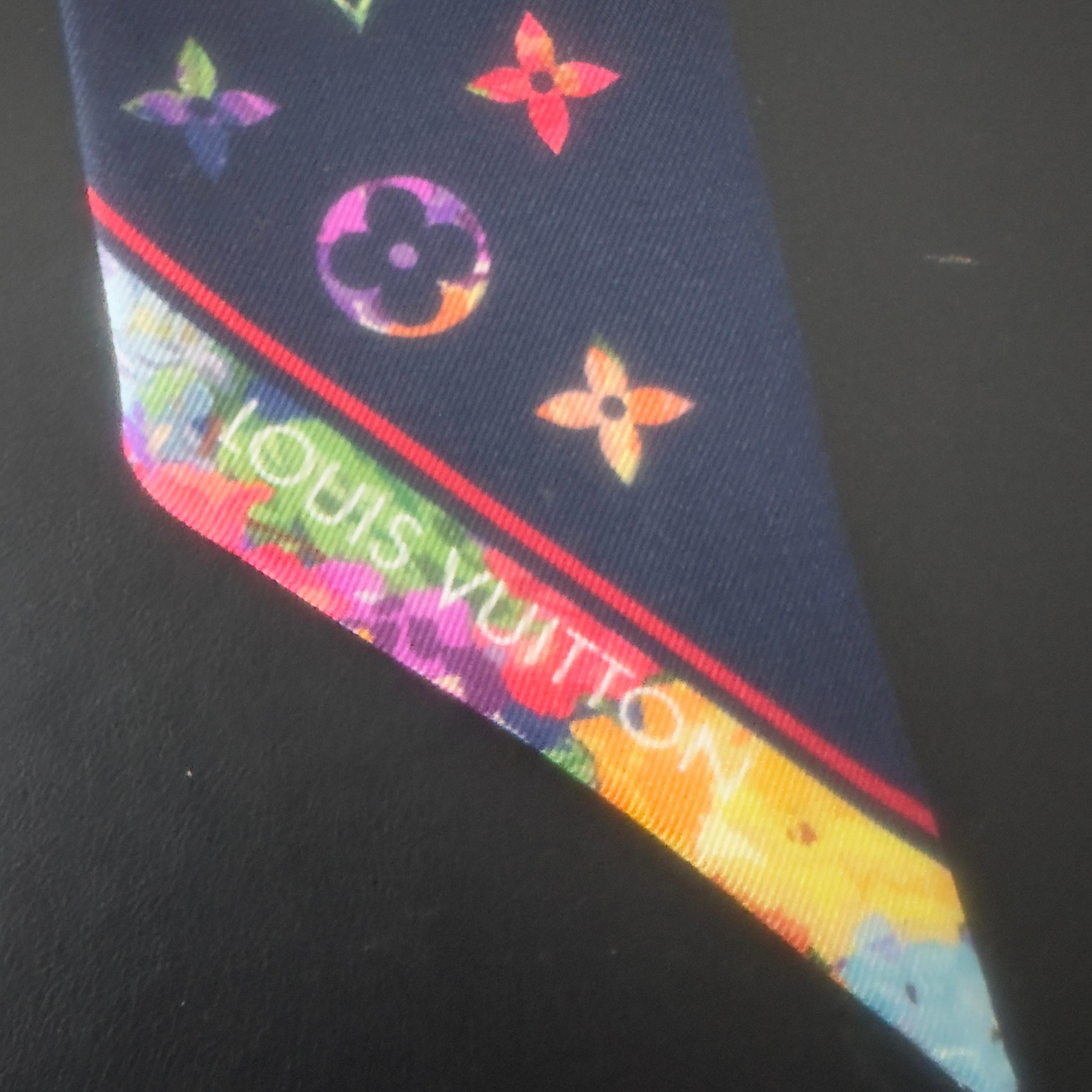 Un piccolo capolavoro firmato Louis Vuitton.
Questo twilly in pura seta è decorato con l’iconico monogramma LV in versione multicolor: un’esplosione di loghi floreali e iniziali in tonalità vivaci, su una base blu navy che ne esalta l’intensità.
Un