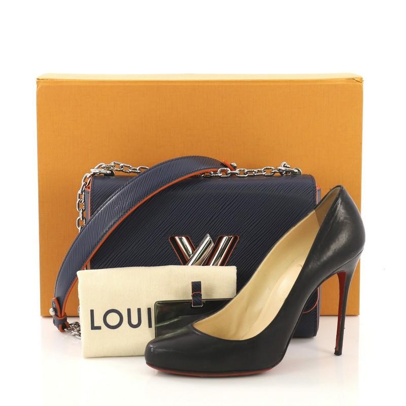 This Louis Vuitton Twist Handbag Epi Leather MM, crafted from navy epi leather, features a chain link strap with leather pad, frontal flap, and silver-tone hardware. Its LV twist lock closure opens to an orange microfiber interior with slip pockets.