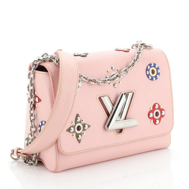 This Louis Vuitton Twist Handbag Limited Edition Mechanical Flowers Epi Leather MM, crafted from pink epi leather, features chain link strap with leather pad, multicolor flowers with circular studs, and silver-tone hardware. Its LV twist-lock