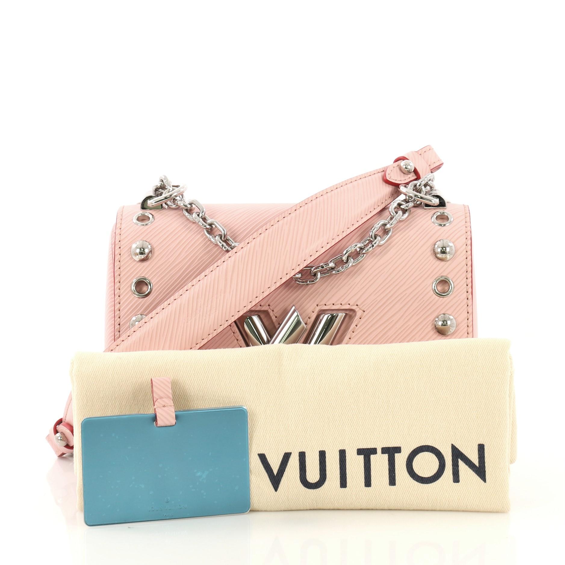 This Louis Vuitton Twist Handbag Studded Epi Leather PM, crafted in light pink studded epi leather, features a waved base silhouette, chain link strap with leather pad, and silver-tone hardware. It opens to a light pink microfiber interior with slip