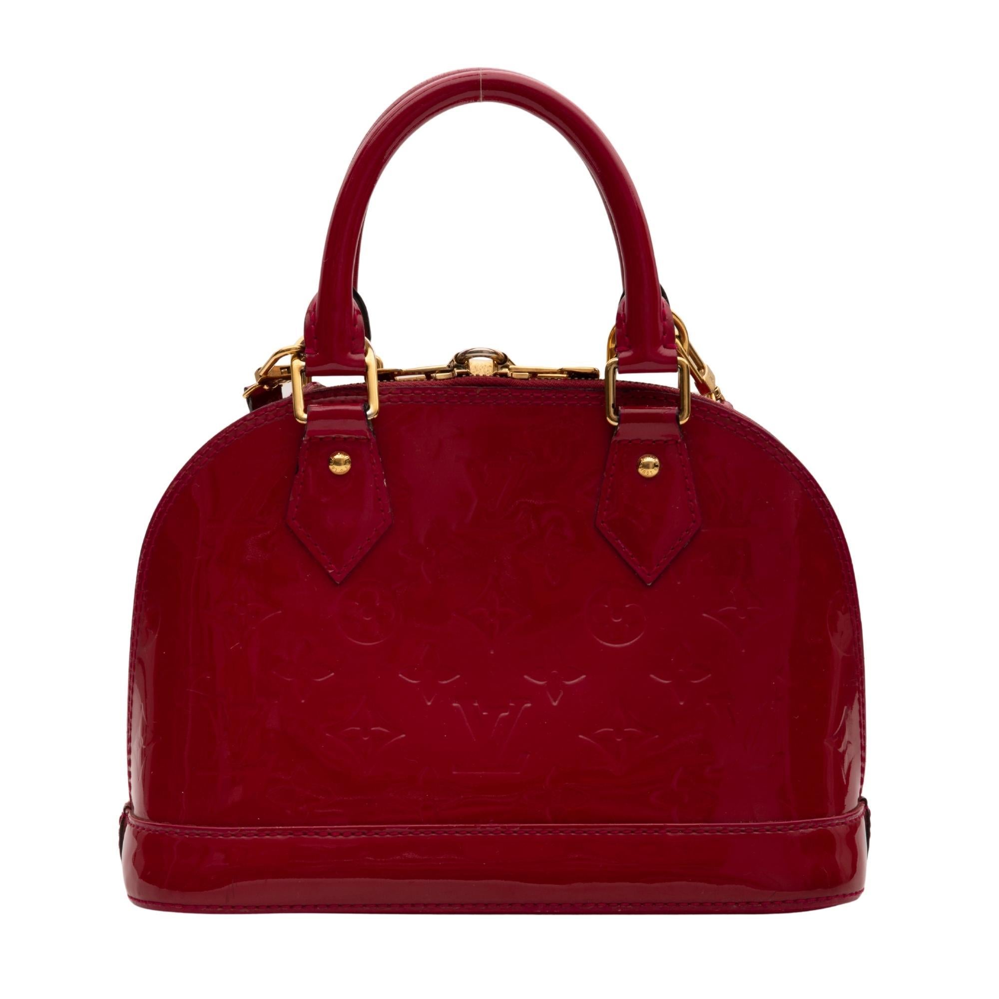 This small Alma is constructed with monogram embossed vernis patent leather in red. The handbag features dual rolled leather top handles, an optional shoulder strap, polished brass hardware, a hanging clochette for the keys, wrap around zip closure