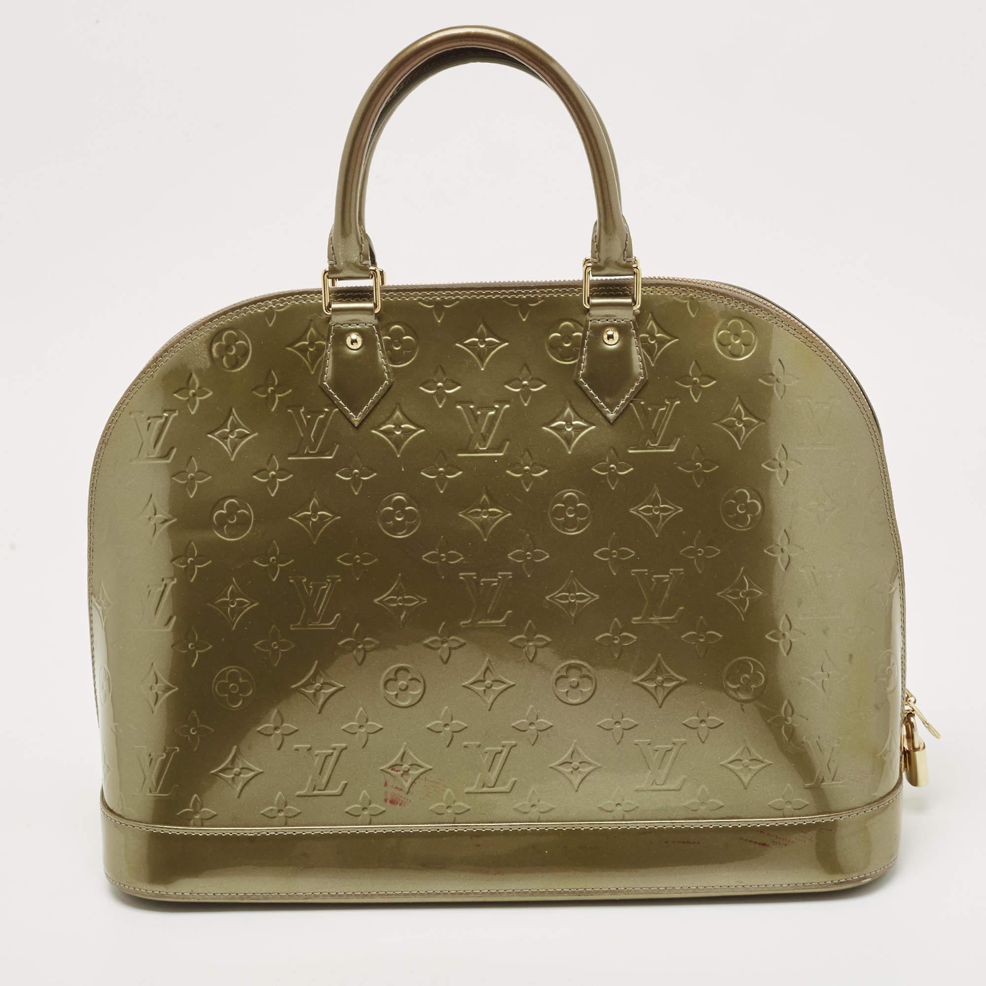 Issu de l'une des collections les plus emblématiques de Louis Vuitton, ce sac Alma est imprégné d'un savoir-faire exquis et de détails historiques. Confectionné en cuir Vert Olive Monogram Vernis, il est doté de deux poignées sur le dessus, d'une
