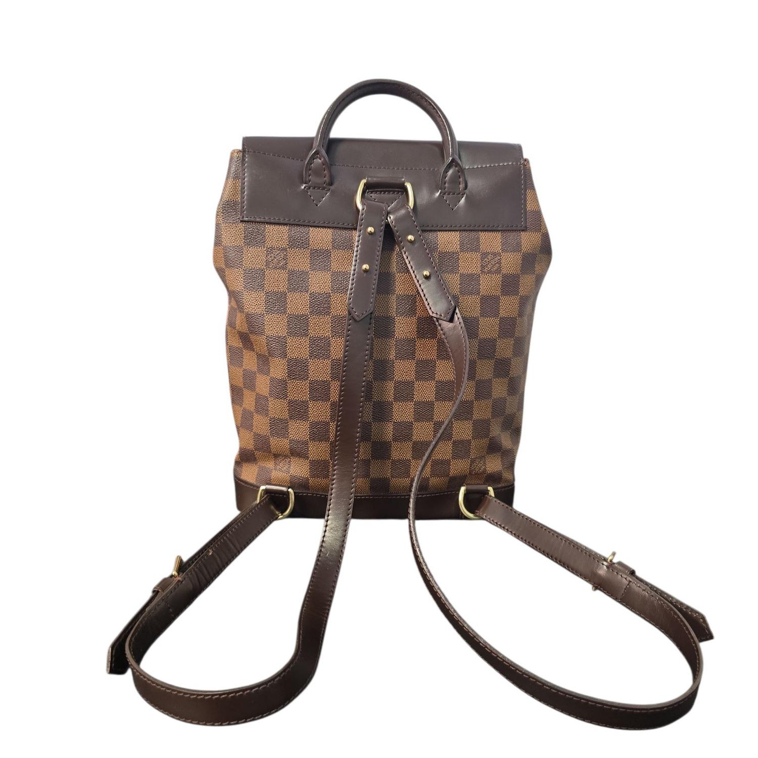 Ce sac à dos Louis Vuitton Vintage Damier Ebene Soho, fabriqué en juin 1998 en France, présente l'emblématique toile enduite de la marque dans un riche motif de damier marron et tan. Doté de solides accessoires en laiton doré, d'une fermeture à