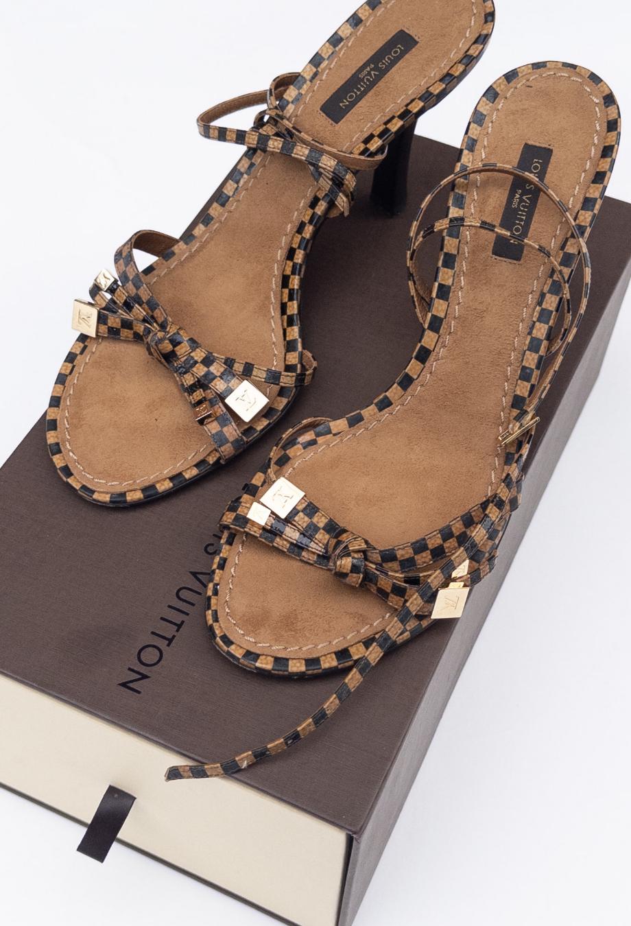 Ces talons à bride de cheville Louis Vuitton sont confectionnés dans le cuir verni Damier, signature de la maison, et dotés d'une assise plantaire en daim souple pour plus de confort et de contraste. La silhouette à brides enveloppe élégamment le