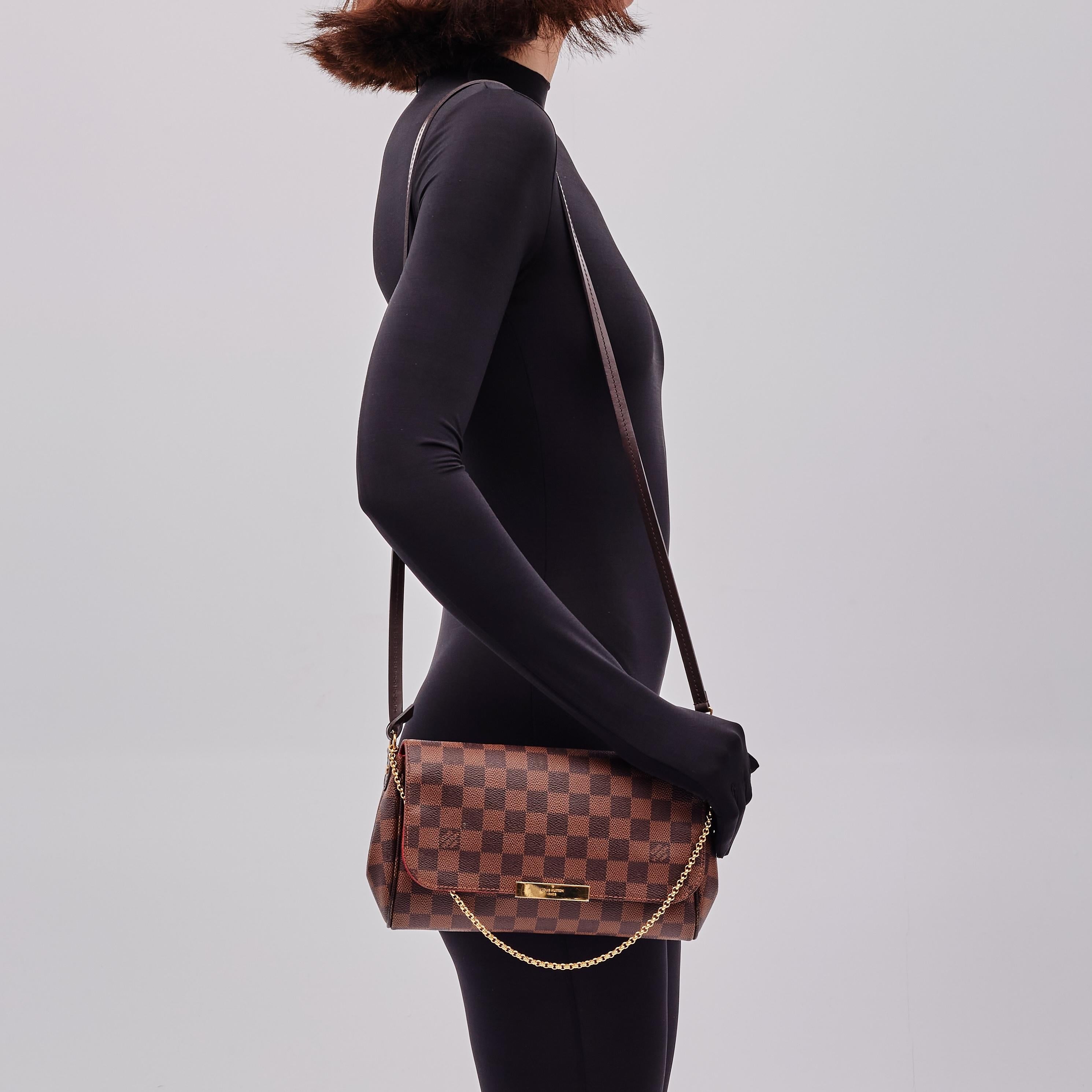 This bag is made of classic Damier toile canvas. The shoulder bag features a polished brass chain-link wristlet strap and an optional brown leather crossbody strap. The crossover flap opens with a magnetic brass bar to a fabric interior with a patch