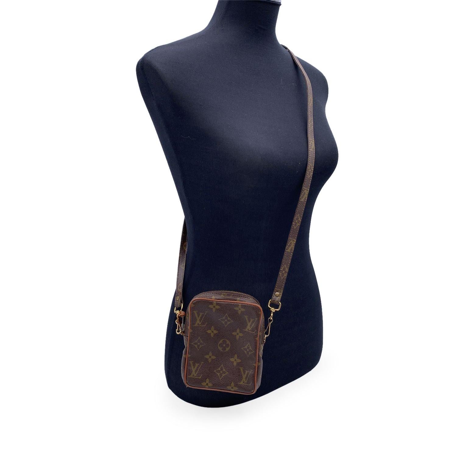 Stylish 'Mini Danube' Crossbody camera bag beautifully crafted in timeless monogram canvas. The bag features tan leather trim, a cross body strap with gold metal hardware. The top zipper opens to a leather interior. Monogram shoulder strap. 'LOUIS