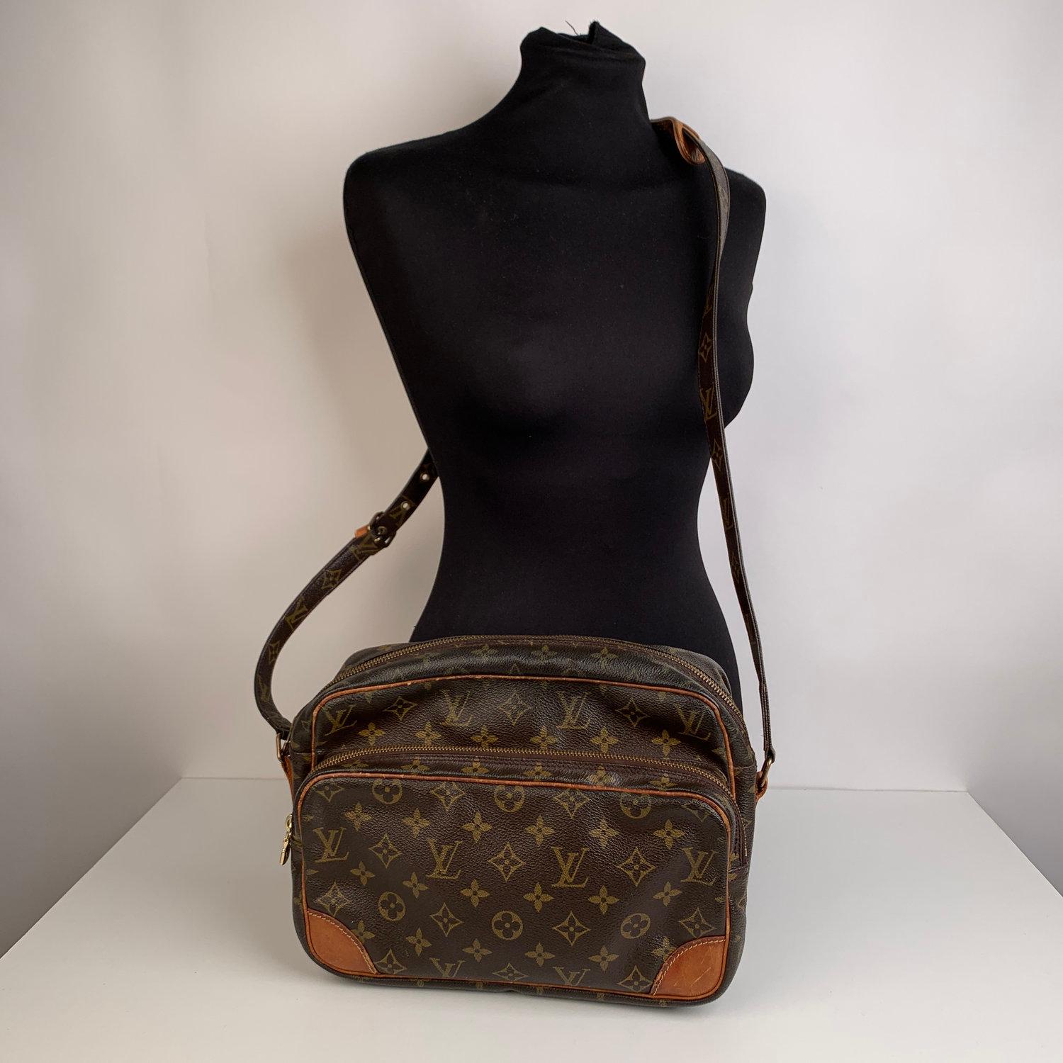 LOUIS VUITTON 'Nil' crafted in timeless monogram canvas with vacchetta leather trim. It features 1 zip pocket on the front, golden brass hardware and adjustable canvas shoulder strap. Zip closure on top. Inside it is linined with leather and 1 side