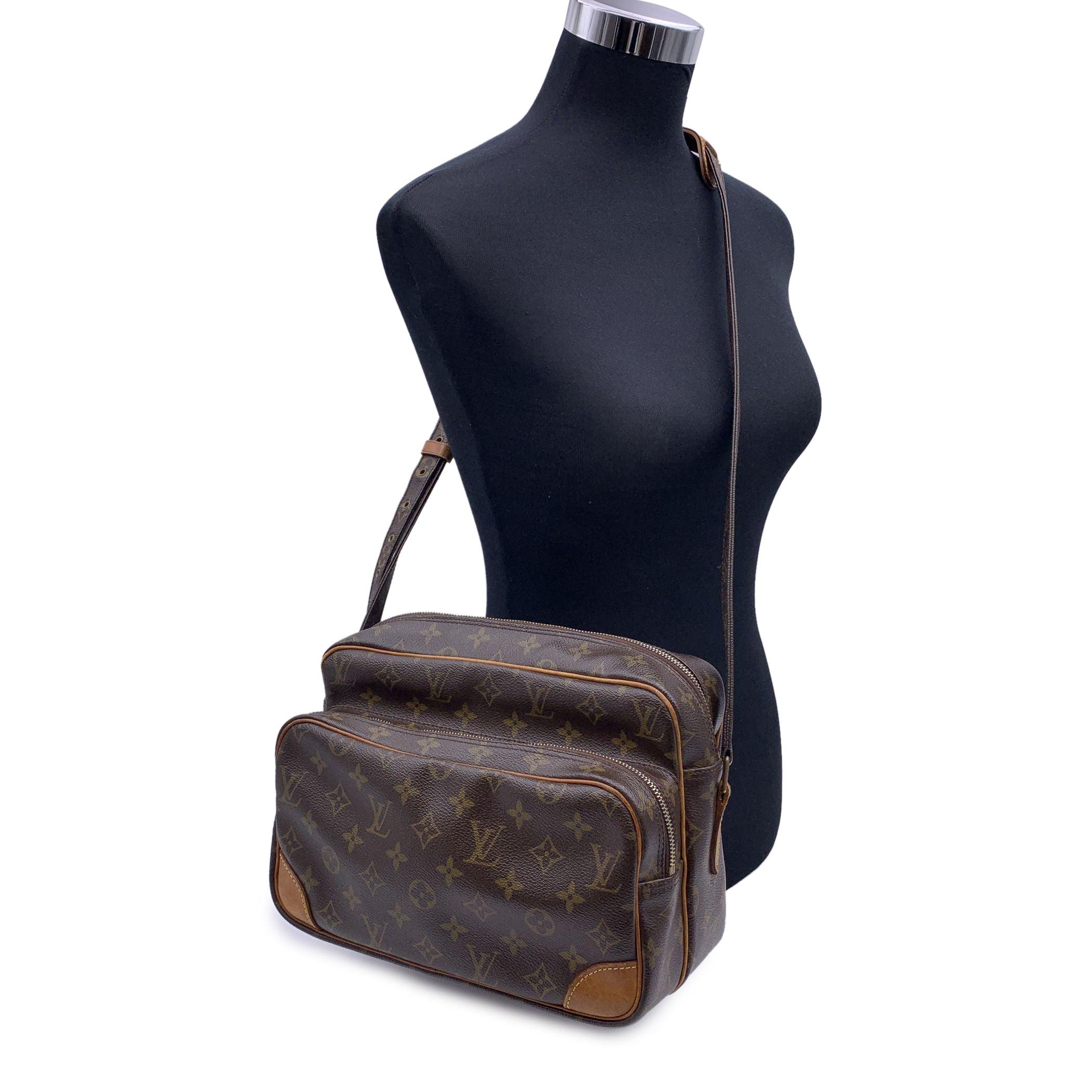 LOUIS VUITTON 'Nil' crafted in timeless monogram canvas with vacchetta leather trim. It features 1 zip pocket on the front, golden brass hardware and adjustable canvas shoulder strap. Zip closure on top. Inside it is lined with leather and 1 side