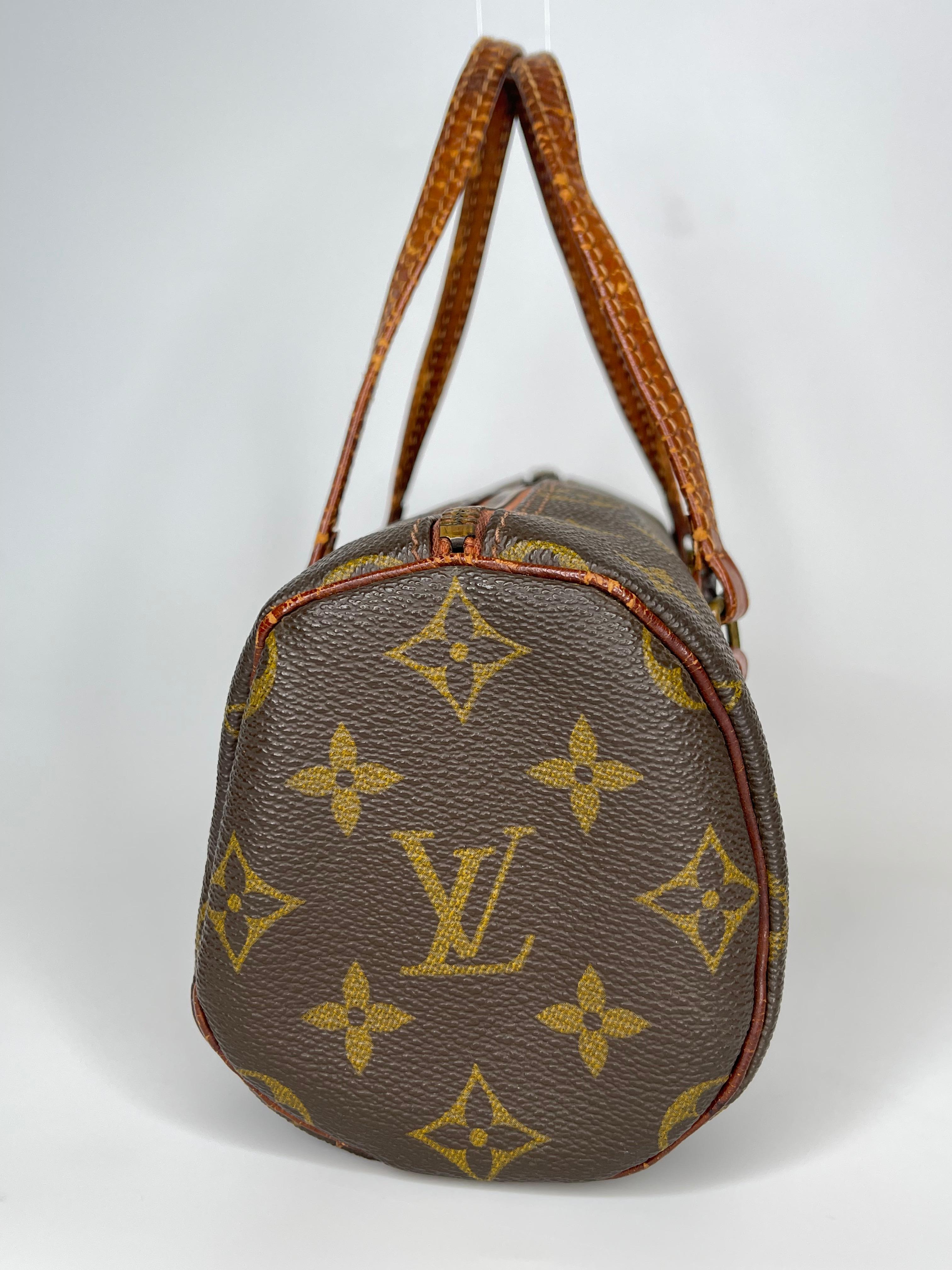 Este mini bolso vintage mide 22 cm de largo y está confeccionado con lona revestida marrón con estampado de monograma y remates y acabados de cuero natural color caramelo envejecido.  El bolso tiene un interior de piel de cerdo y una cremallera en