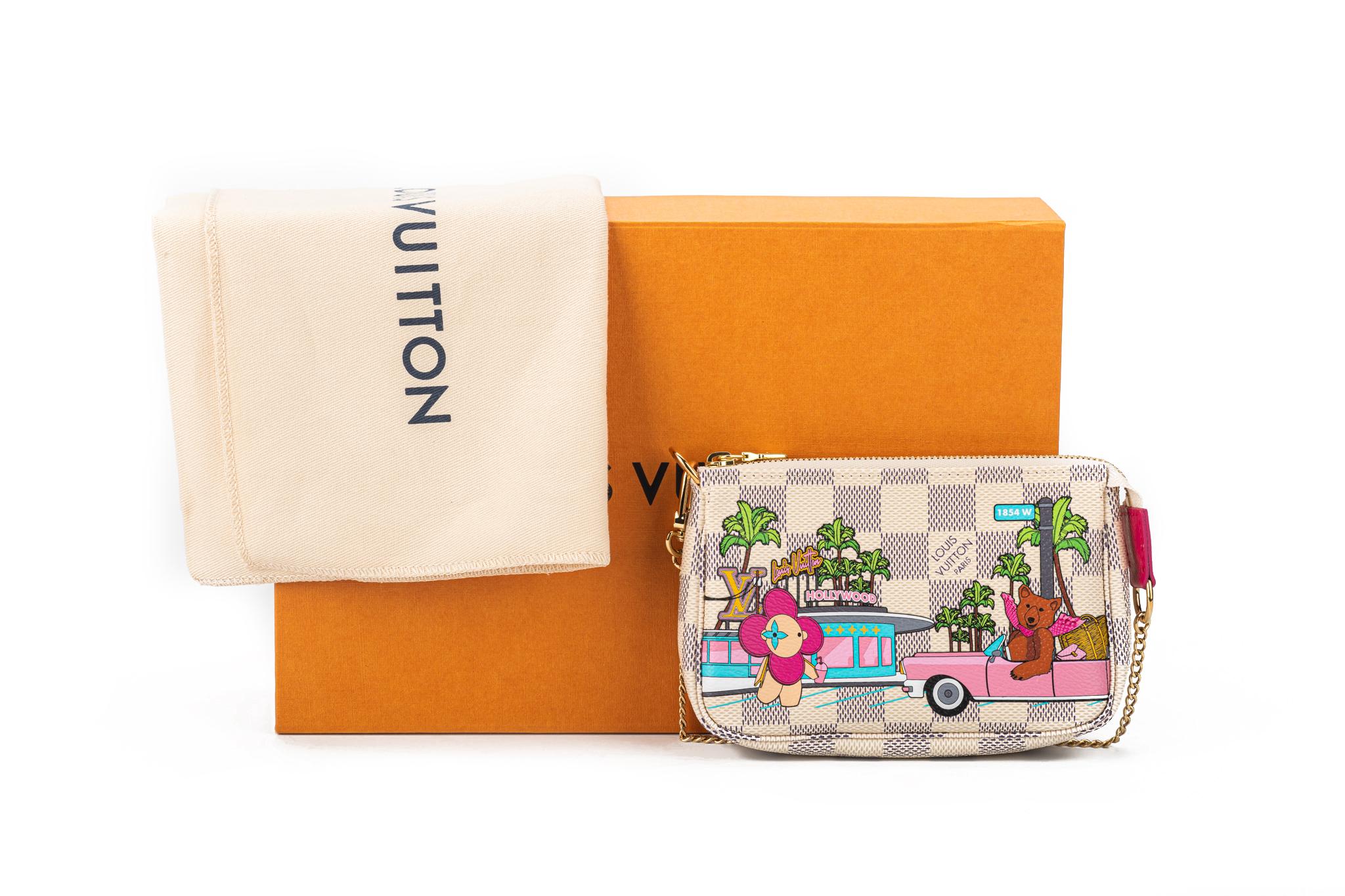Louis Vuitton Mini Pochette Accessoires In White Crafted from Damier Azur canvas. The Mini Pochette features a limited edition print of the house mascot Vivienne visiting Hollywood. In front of the LV Diner, she watches as a California bear arrives