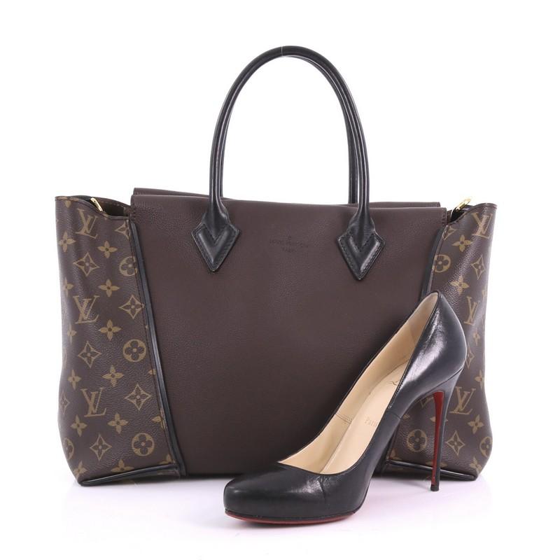 This Louis Vuitton W Tote Monogram Canvas and Leather PM, crafted in brown monogram coated canvas and leather, features dual rolled handles, protective base studs, and gold-tone hardware. It opens to a brown suede interior with side zip and slip