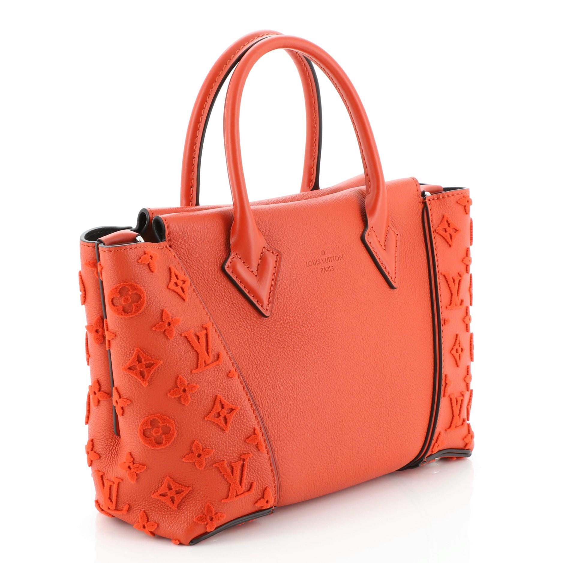 This Louis Vuitton W Tote Veau Cachemire Calfskin BB, crafted from red veau cachemire calfskin leather, features dual rolled handles, expansive sides with tufted monogram embossed patterns, and silver-tone hardware. Its magnetic snap closure opens