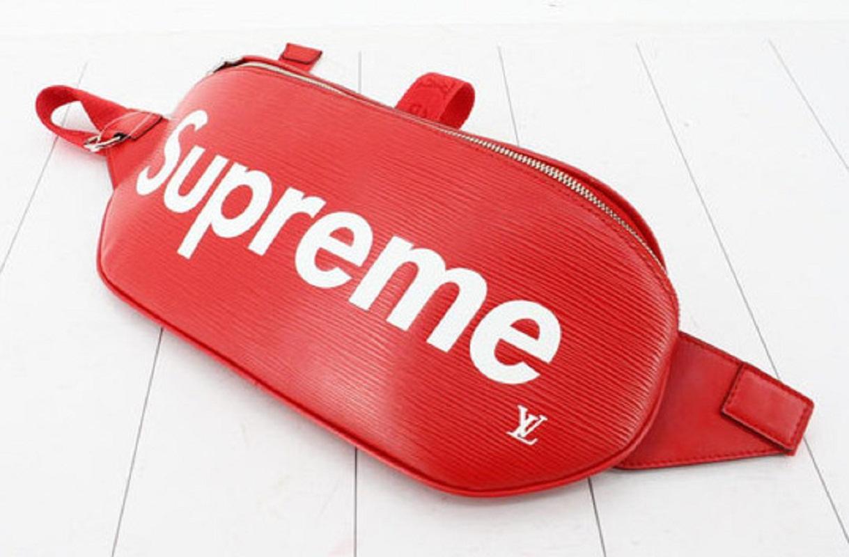 Men's red Epi leather Louis Vuitton x Supreme Bum bag with silver-tone hardware, single canvas waist strap with buckle closure, logo printed at front face, black Alcantara lining and zip closure at front.

 

61304MSC