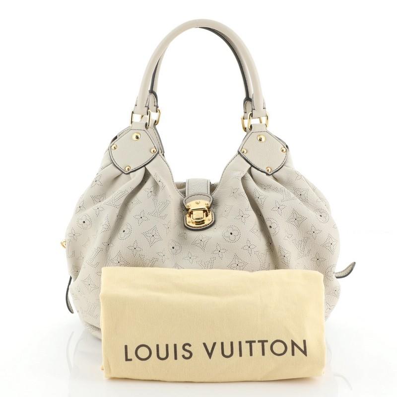 This Louis Vuitton XL Hobo Mahina Leather, crafted from neutral monogram perforated mahina leather, features dual rolled handles, buckle and stud details, side belt strap closures, protective base studs, and gold-tone hardware. Its engraved top flap