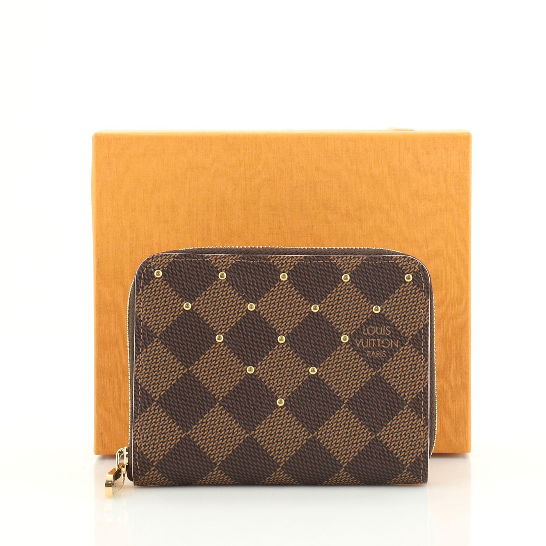 This Louis Vuitton Zippy Coin Purse Studded Damier, crafted in damier ebene studded coated canvas, features gold-tone hardware. Its all-around zip closure opens to a pink leather interior with multiple card slots and slip pockets. Authenticity code