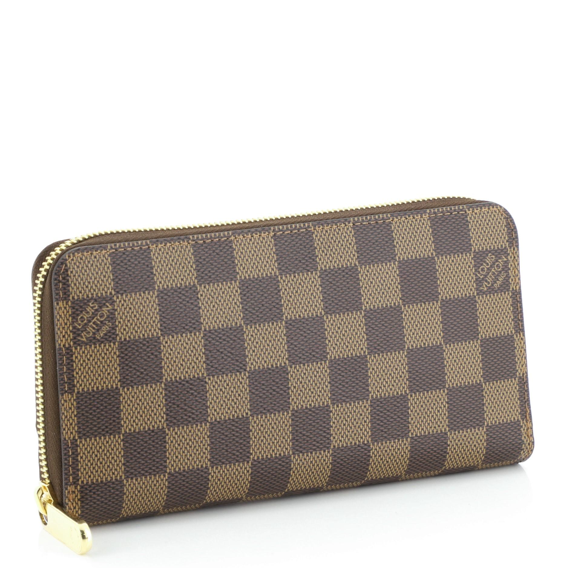 This Louis Vuitton Zippy Wallet Damier, crafted from damier ebene coated canvas, features gold-tone hardware. Its all-around zip closure opens to a pink leather interior with multiple card slots, two gusseted open pockets, and zip pocket.