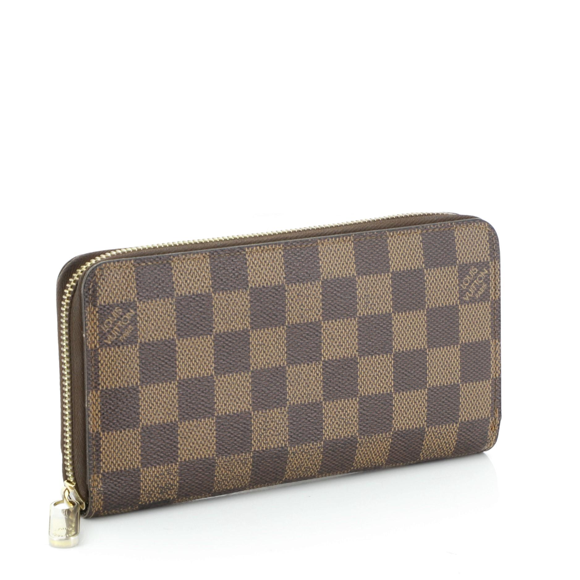 This Louis Vuitton Zippy Wallet Damier, crafted from damier ebene coated canvas, features gold-tone hardware. Its all-around zip closure opens to a brown leather interior with multiple card slots, two gusseted open pockets, and zip pocket.