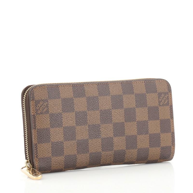 This Louis Vuitton Zippy Wallet Damier, crafted from damier ebene coated canvas, features gold-tone hardware. Its all-around zip closure opens to a brown leather interior with multiple card slots, two gusseted open pockets, and zip pocket.