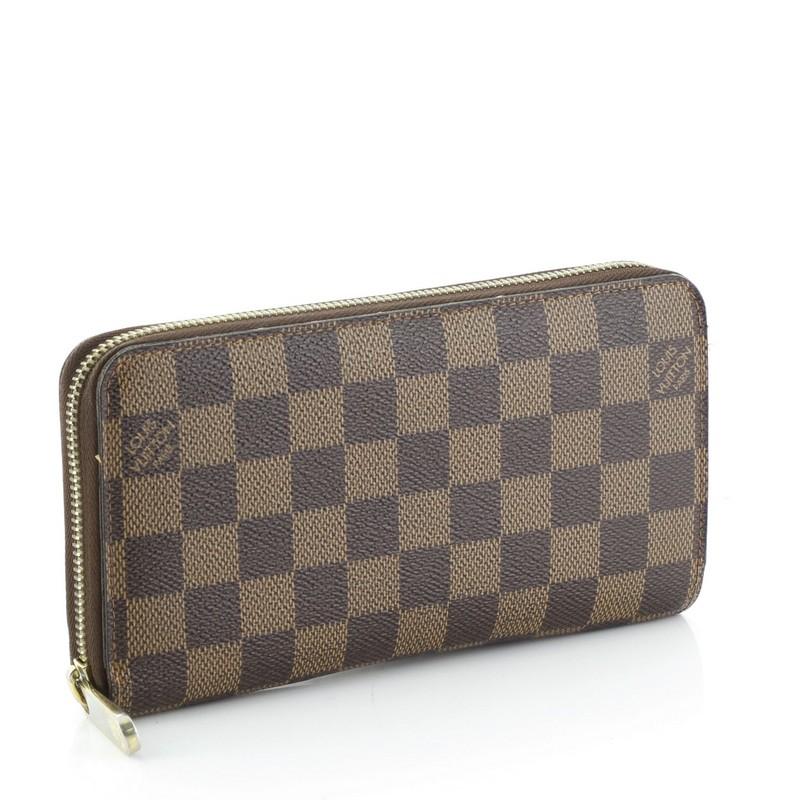 This Louis Vuitton Zippy Wallet Damier, crafted from damier ebene coated canvas, features gold-tone hardware. Its all-around zip closure opens to a brown leather interior with multiple card slots, two gusseted open pockets, and zip pocket.