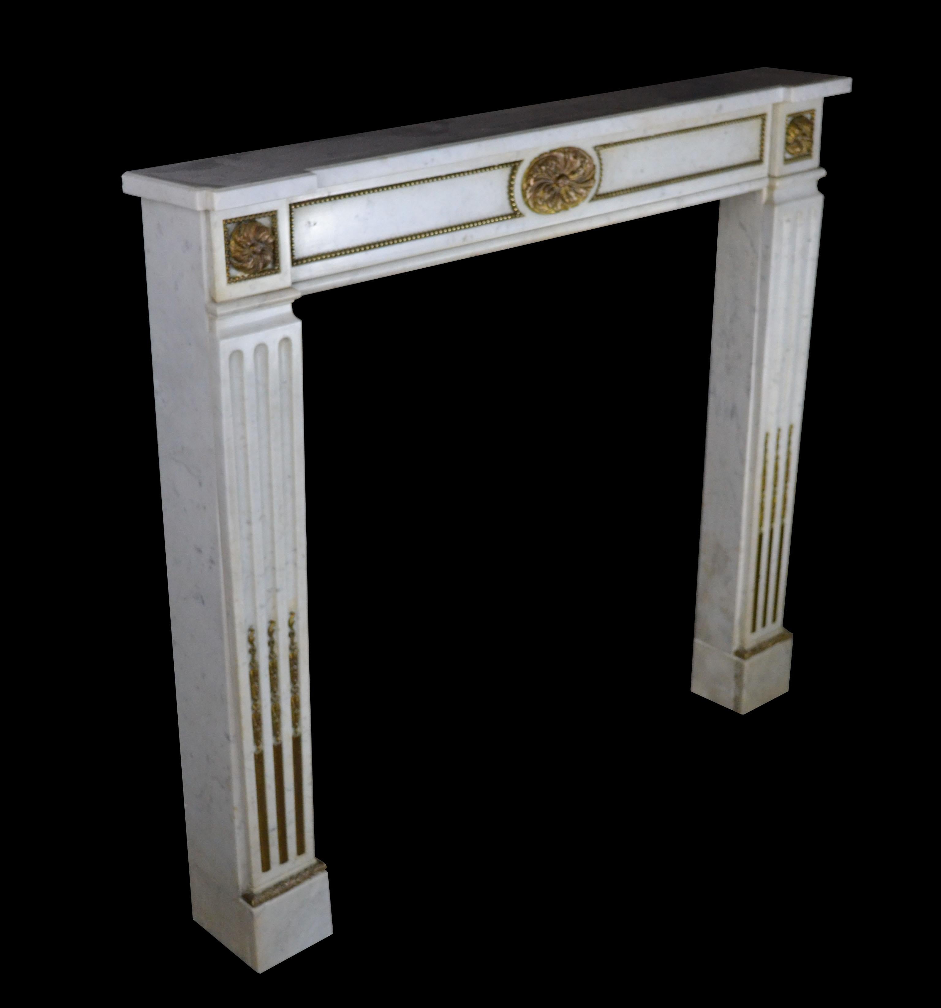 A 19th century French mantel in the style of Louis VXI in Carrara marble with stop fluted tapering console jambs inset with ormolu terminating beneath corner blocks with Ormolu rosettes, the frieze with a central elliptical ormolu rosette flanked by