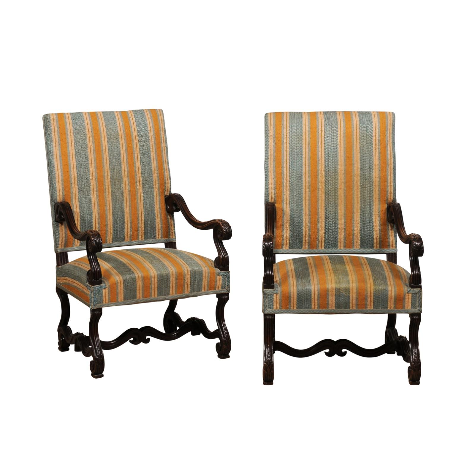 A pair of French Louis XIII style os de mouton carved walnut armchairs from the 19th century with large scrolling arms. Behold the timeless elegance of this pair of French Louis XIII style Os de Mouton armchairs, dated back to the 19th Century.