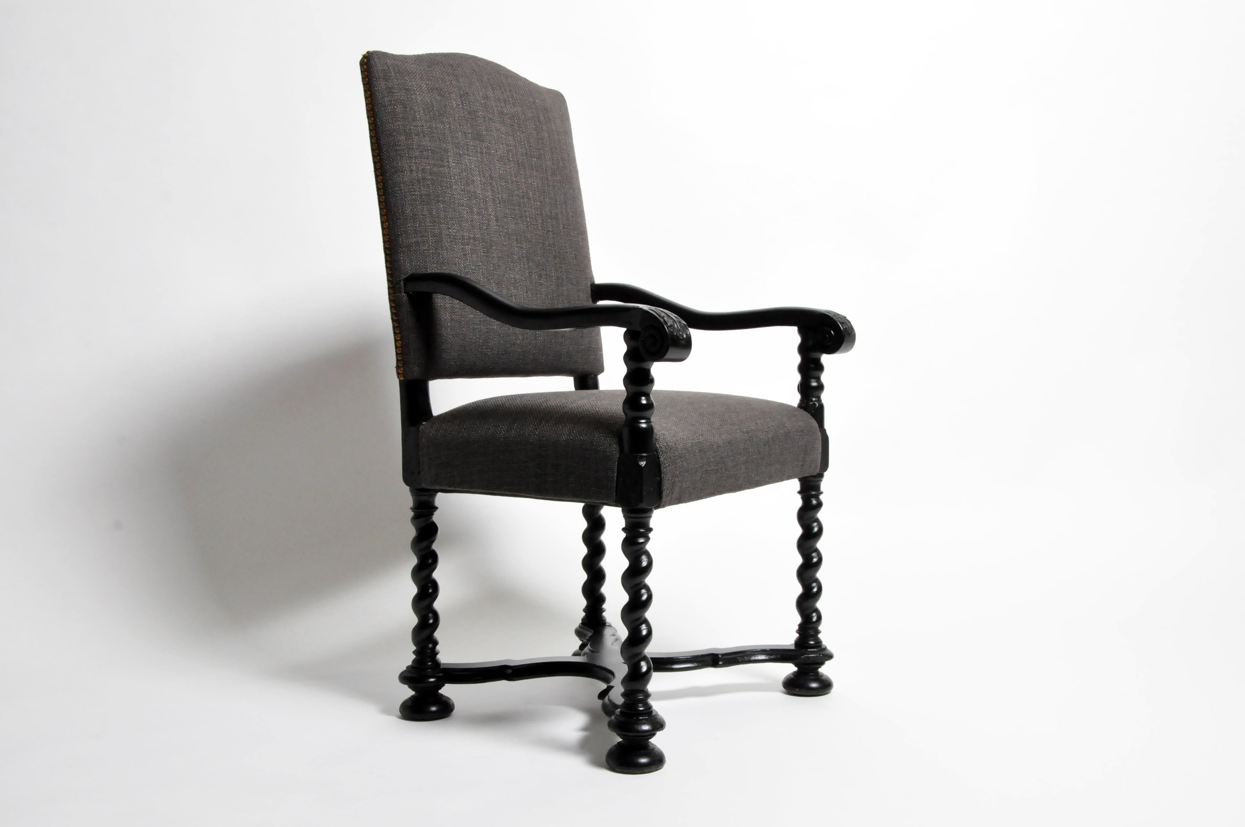This carved armchair has an arched and padded back upholstered in burlap-like fabric with nailhead decoration. The exposed Walnut frame features scrolled arms on turned supports that continue down into barley twist legs raised on ball, joined by an