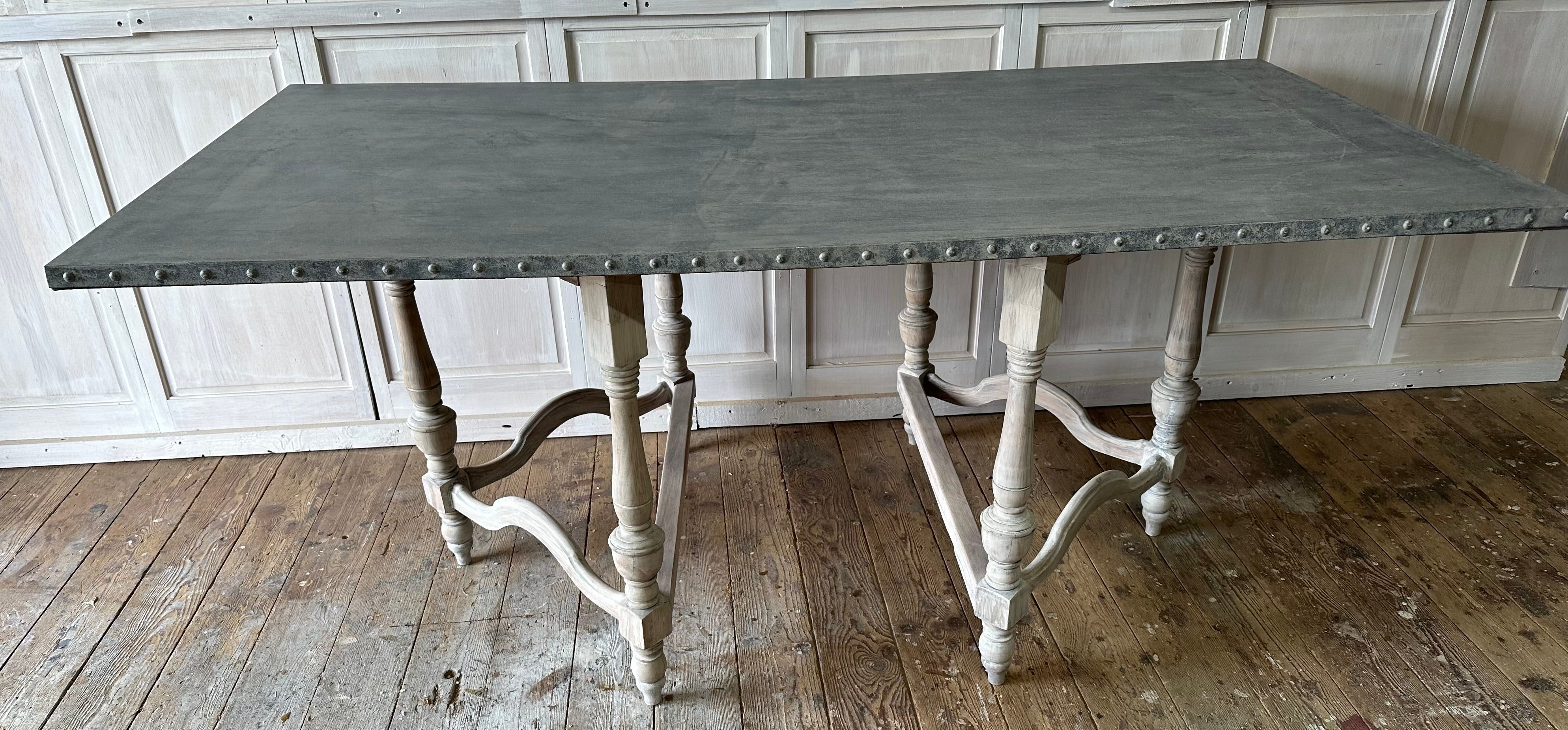 A marriage of style and functionality -- the zinc top sits on an antique hand carved French Louis XIII style white washed table base made circa 1910. The oak Jacobean style base consists of 2 separate three-legged carved wood pedestals.  The