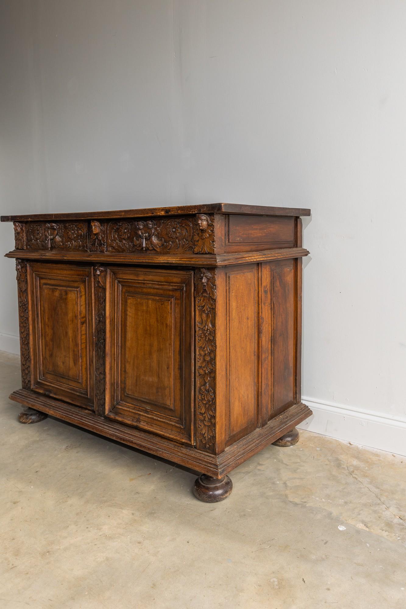 This walnut buffet is a truly beautiful and one of a kind piece. The hand carved details are stunning and the finish of the stain gives this chest a dark and moody feel. There are 3 faces hand carved across the top front of the chest, and there are