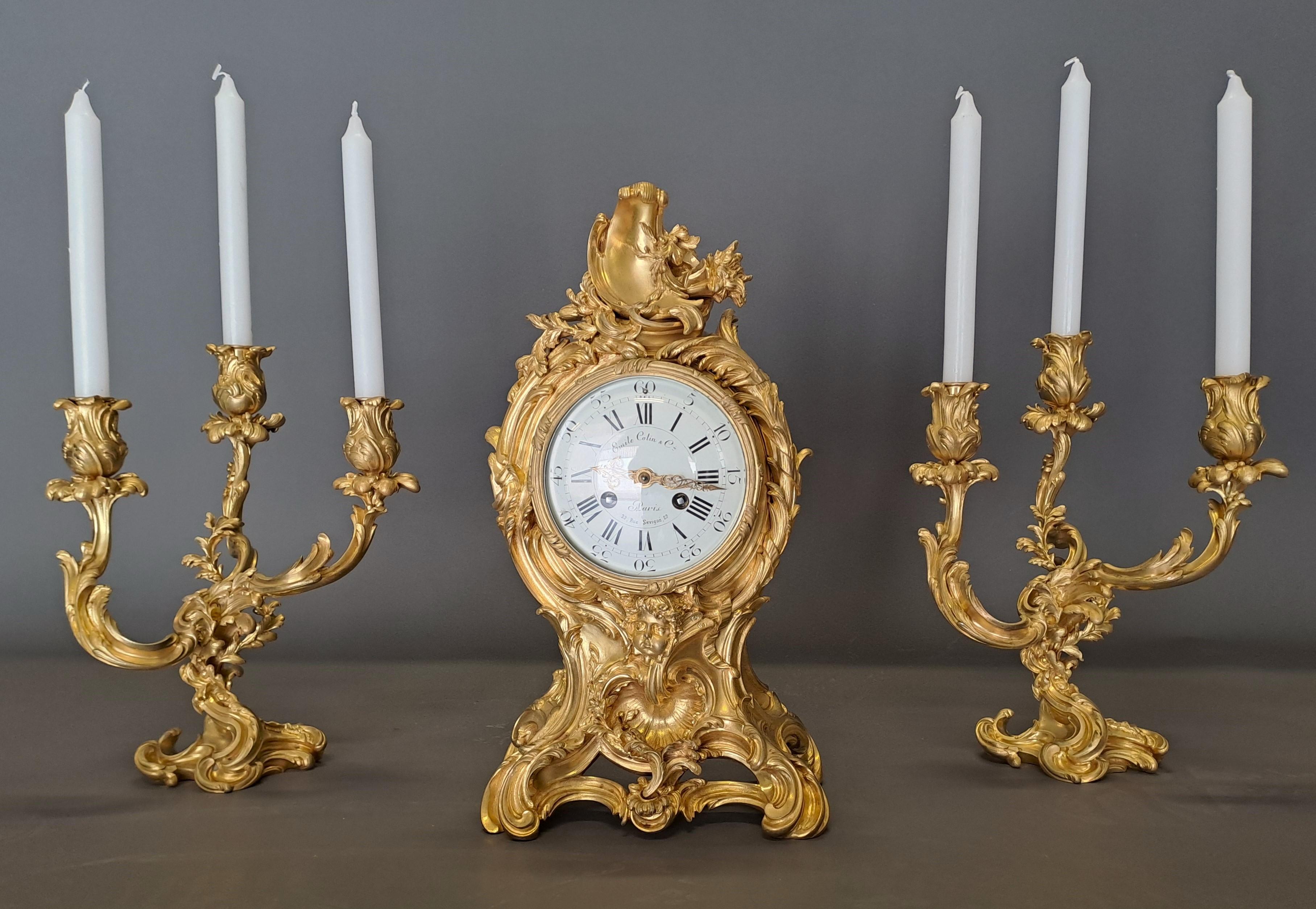 Superb set in very finely chiseled gilded bronze composed of a clock and two candelabras.

Set very richly decorated with motifs inspired by Louis XIV and the Regency, signed on the enameled dial by the house Emile Colin & Cie in Paris.

Very good