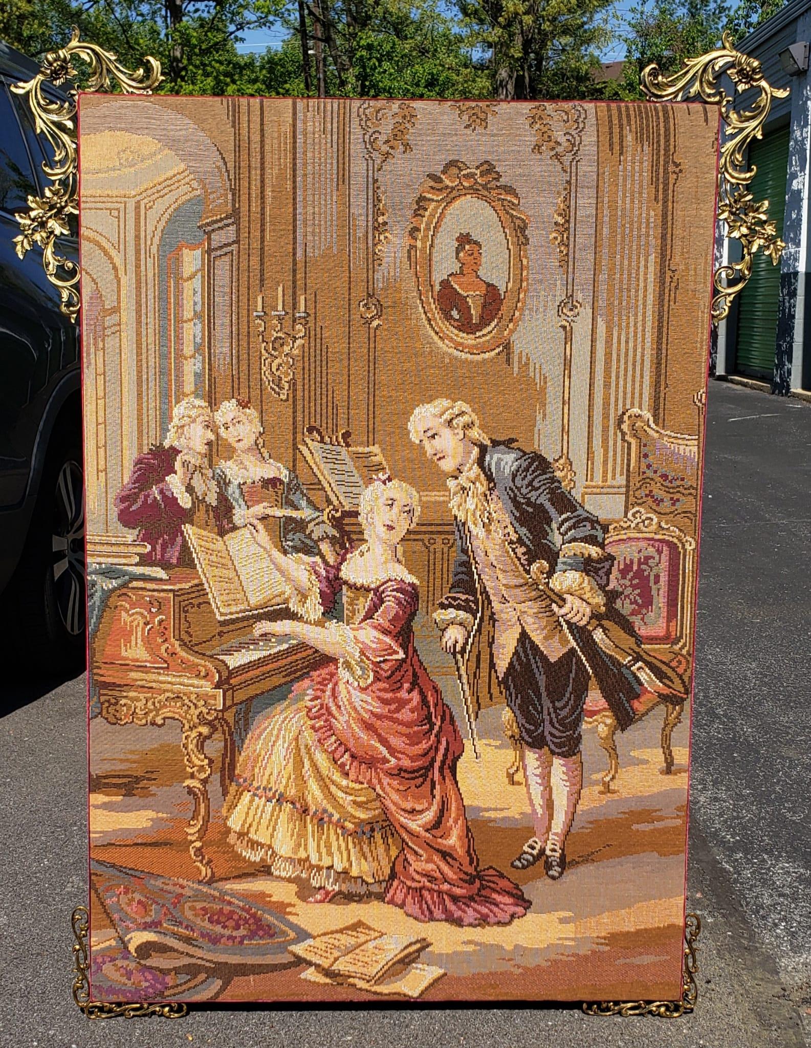 An absolutely gorgeous Louis XIV style Brass Ormolu Mounted and Framed wool Handvoven Tapestry. Tapestry depicts an music room / orchestra scene with a young lady / organ or piano player sitting behind her instrument with a maestro addressing her.