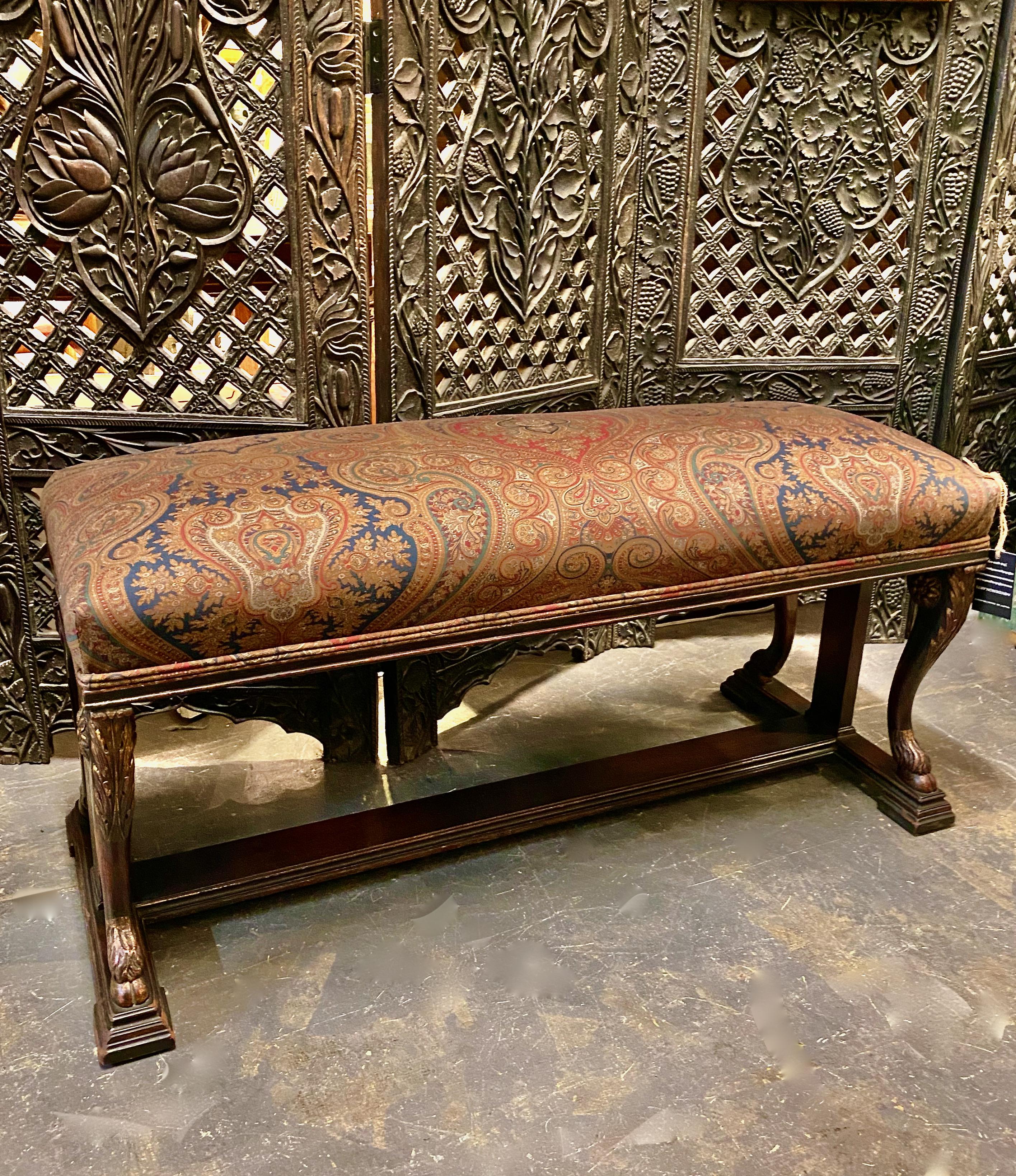 This a good example of an early 20th century Louis XIV or baroque style upholstered bench. The mahogany bench is carved in a masculine form with hairy hoofed feet, acanthus leaf knees, rosettes and stylized ionic columns. It is newly upholstered in