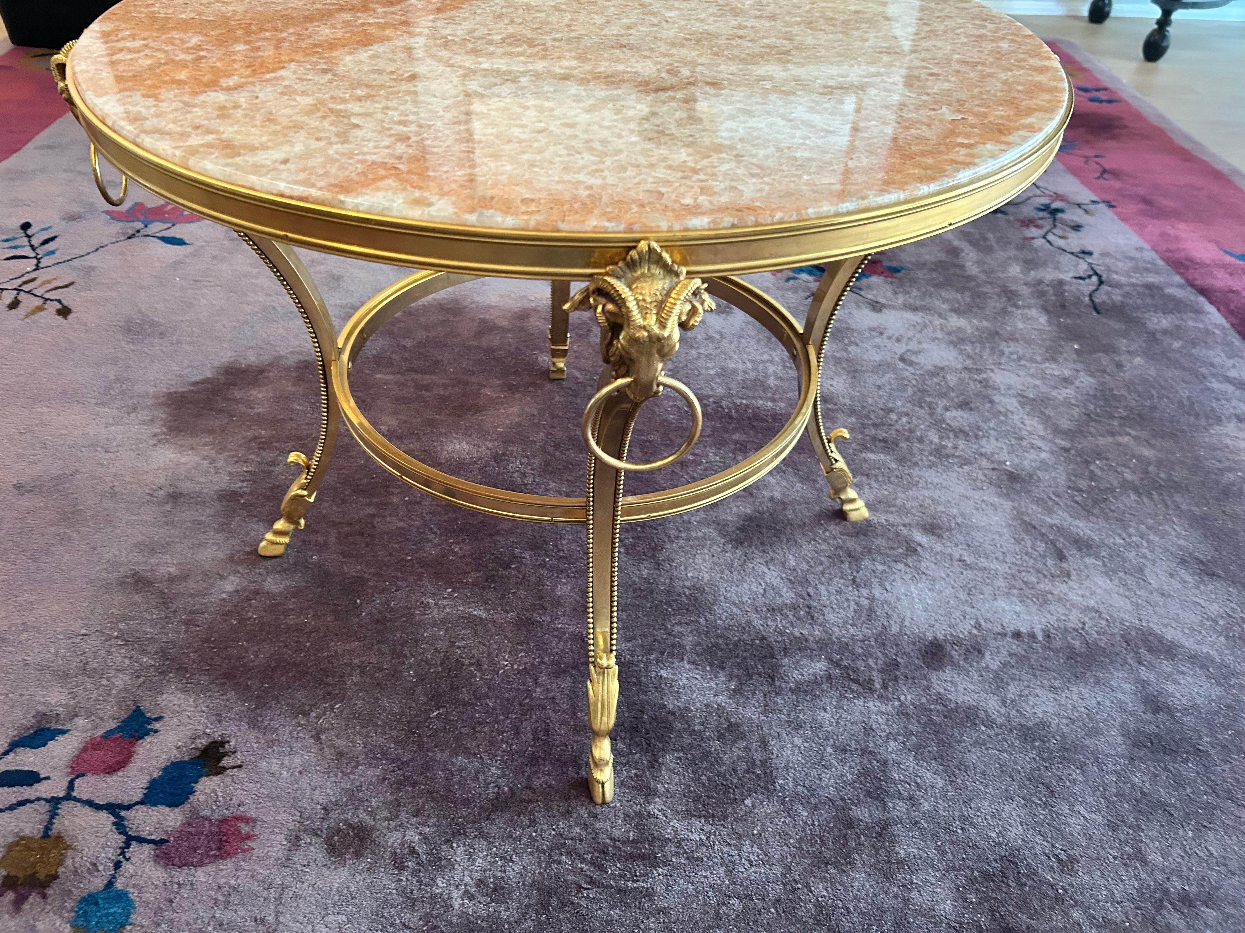 Beautiful Louis XIV style low pedestal table featuring a gilt bronze frame with concave legs terminating in rams' heads with rings, and  elegant hoof feet. The inset top is made of pink/coral onyx.
This table is in pristine condition and would make