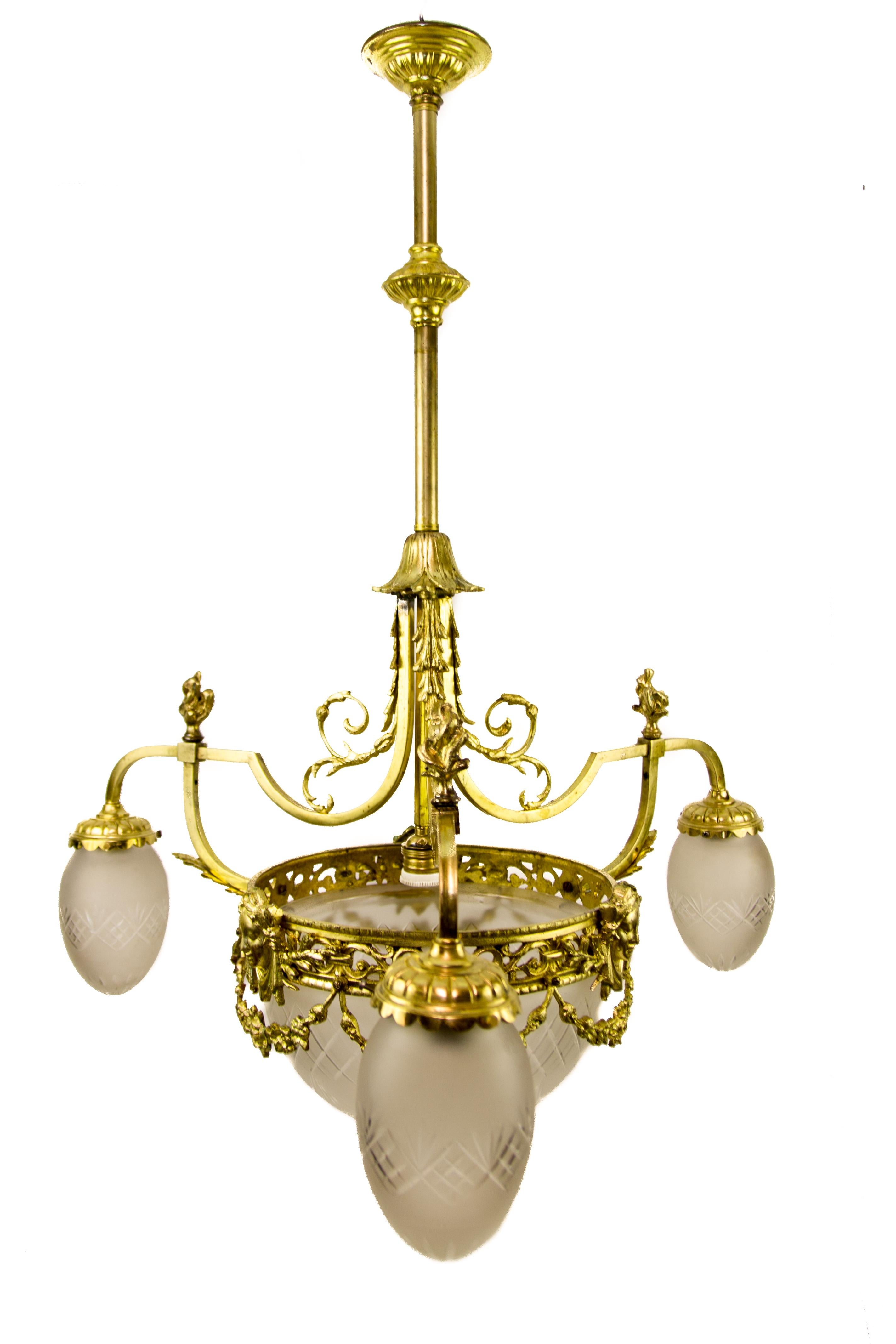 Louis XIV-style gilt bronze chandelier from the 1920s with frosted glass lampshades, ornately decorated with acanthus leaves, flower clusters, and caryatid faces. The antique chandelier has four lights, each with an E27 (E26) size light bulb