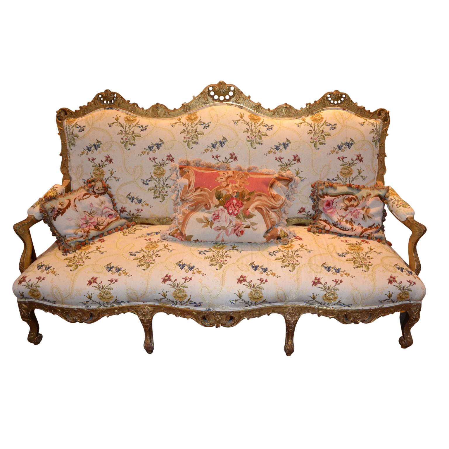 A large scale Louis XIV style open arm settee, the frame in deeply carved and gilded wood. The sculpted frame raised on eight cabriole legs; recently upholstered, (including the back in a sympathetic ivory ground floral fabric).