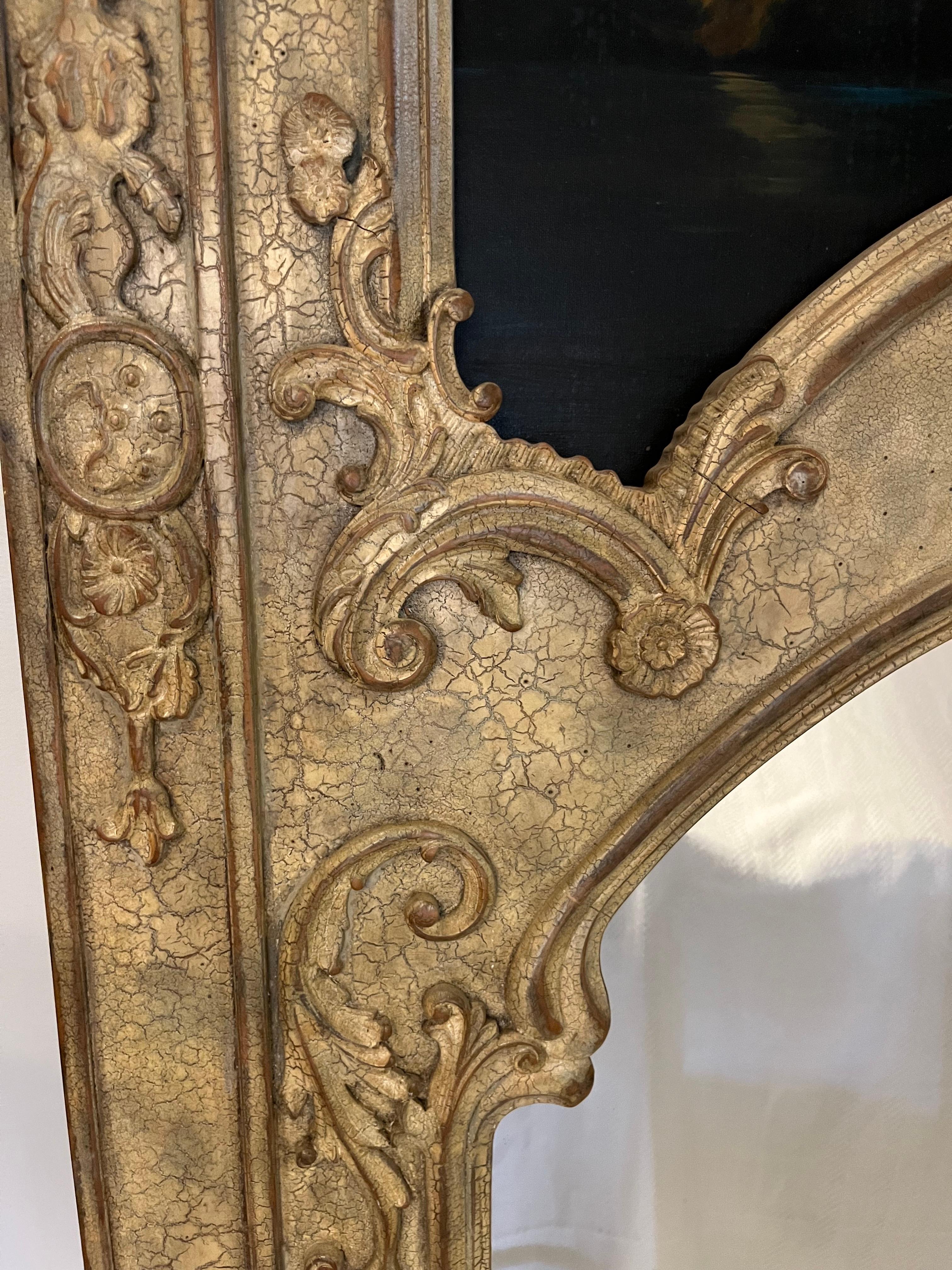 Louis XIV Style Trumeau Mirror with detailed carving, hand painted mural, and framed mirror. The arc at the top of the mirror is accented with shell and foliate details, and sits underneath a desert oasis landscape. The rich painting is enhanced by