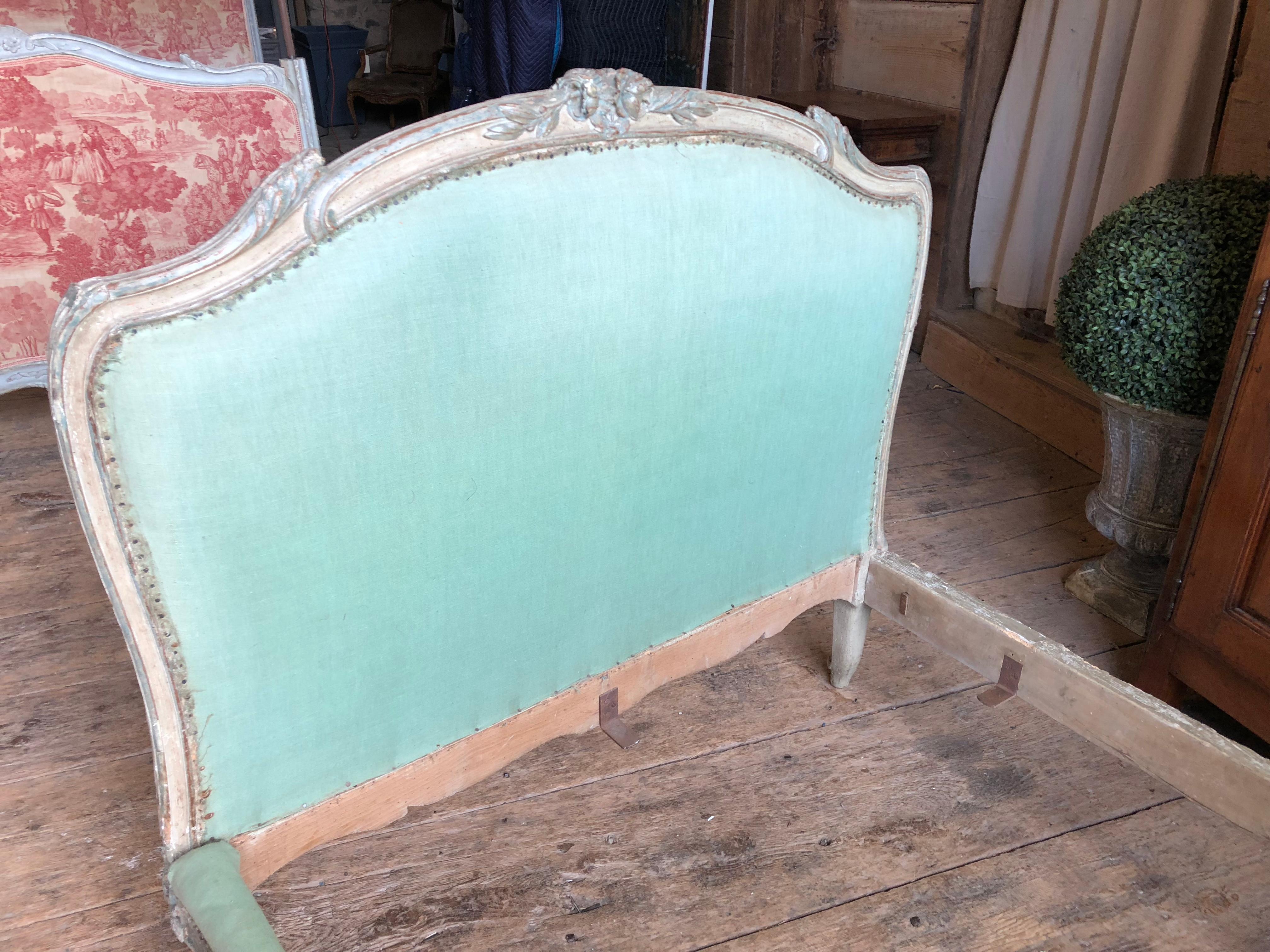 A charming Louis XV period bed, nicely carved and painted cream with blue or green highlights, circa 1760, with upholstered head and footboard, designed to go sideways against the wall, as the front rail is serpentine n shape, while the back rail is