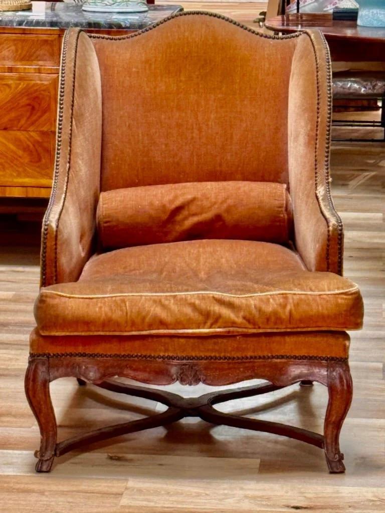 Louis XV beechwood bergère à oreilles, 18th c., First half 18th c., France, the wingback chair with padded back, seat and sides, upholstered in  rust mohair with brass tack edge, above channel carved walnut serpentine apron raised on cabriole legs