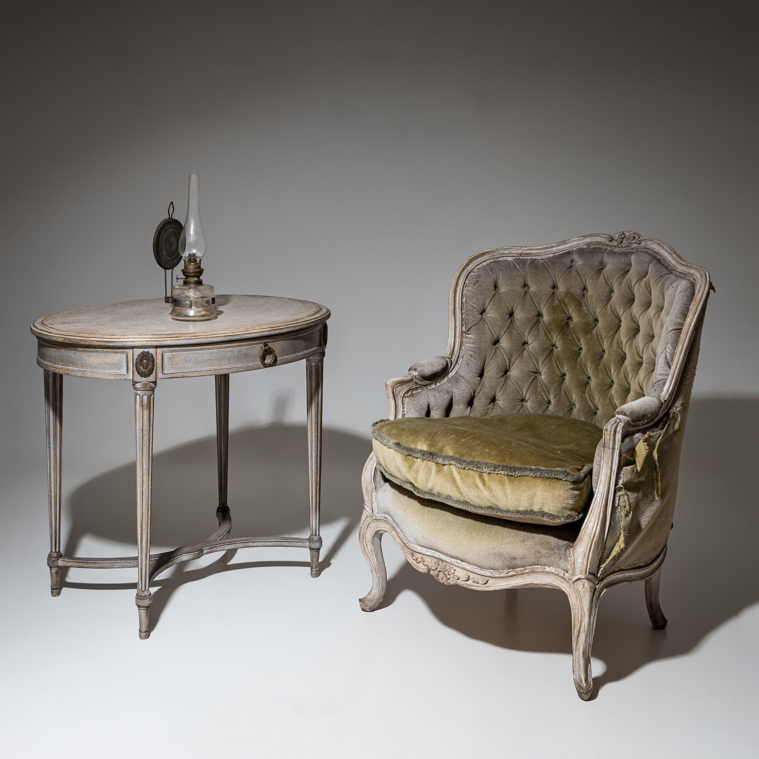 Fauteuil bergère Louis XV du XVIIIe siècle avec un cadre en bois gracieusement courbé et sculpté et une ornementation florale. La tapisserie présente un dossier profondément boutonné et un coussin ample en velours vert olive, montrant des signes