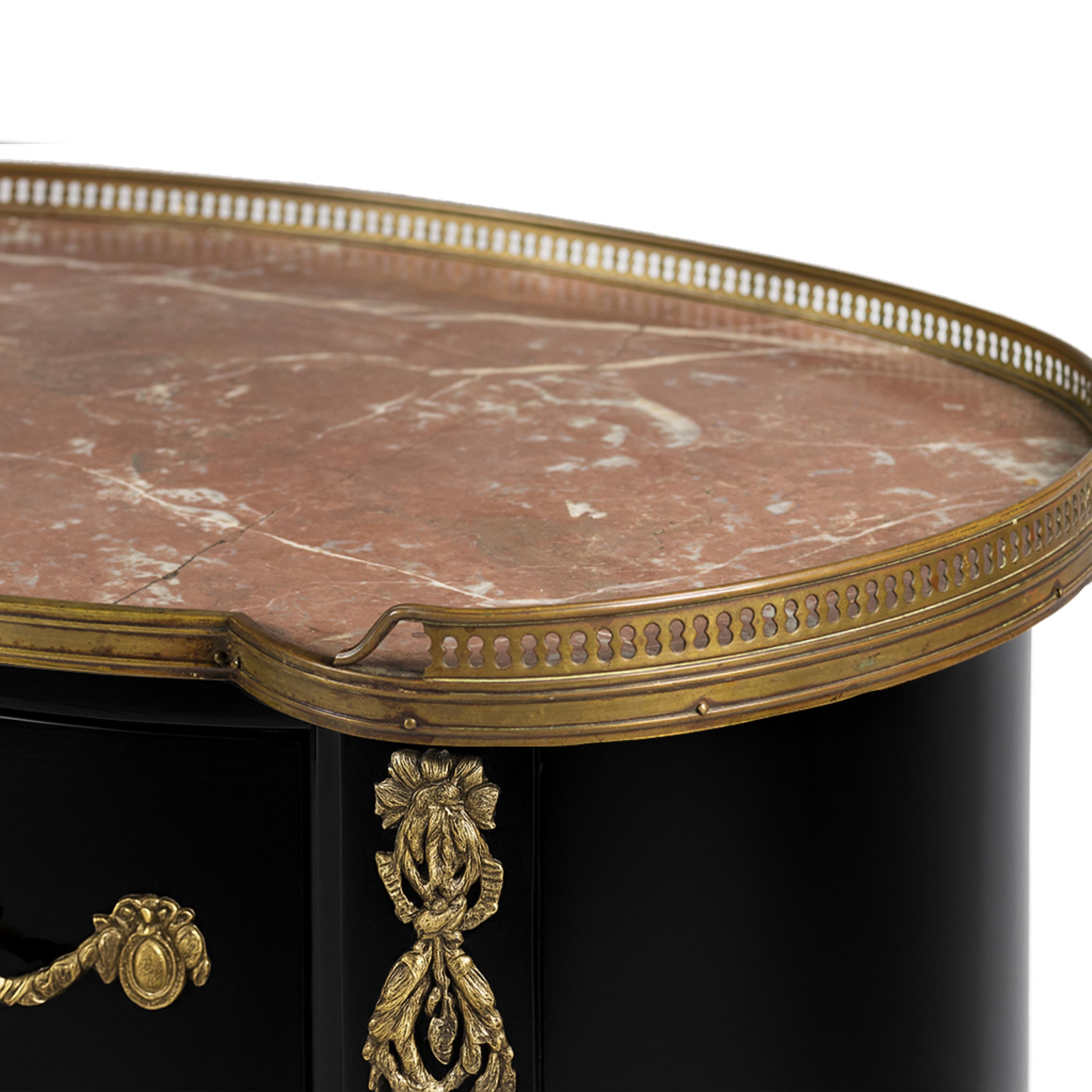 Una commode ovale rifinita in colore nero, un pezzo da comodino di transizione tra lo stile Luigi XV e Luigi XVI.
Tre cassetti, ferramenta e fregi in bronzo dorato. 
Con ringhiere superiori in metallo e intarsi in marmo rosa Cedro proveniente dalle