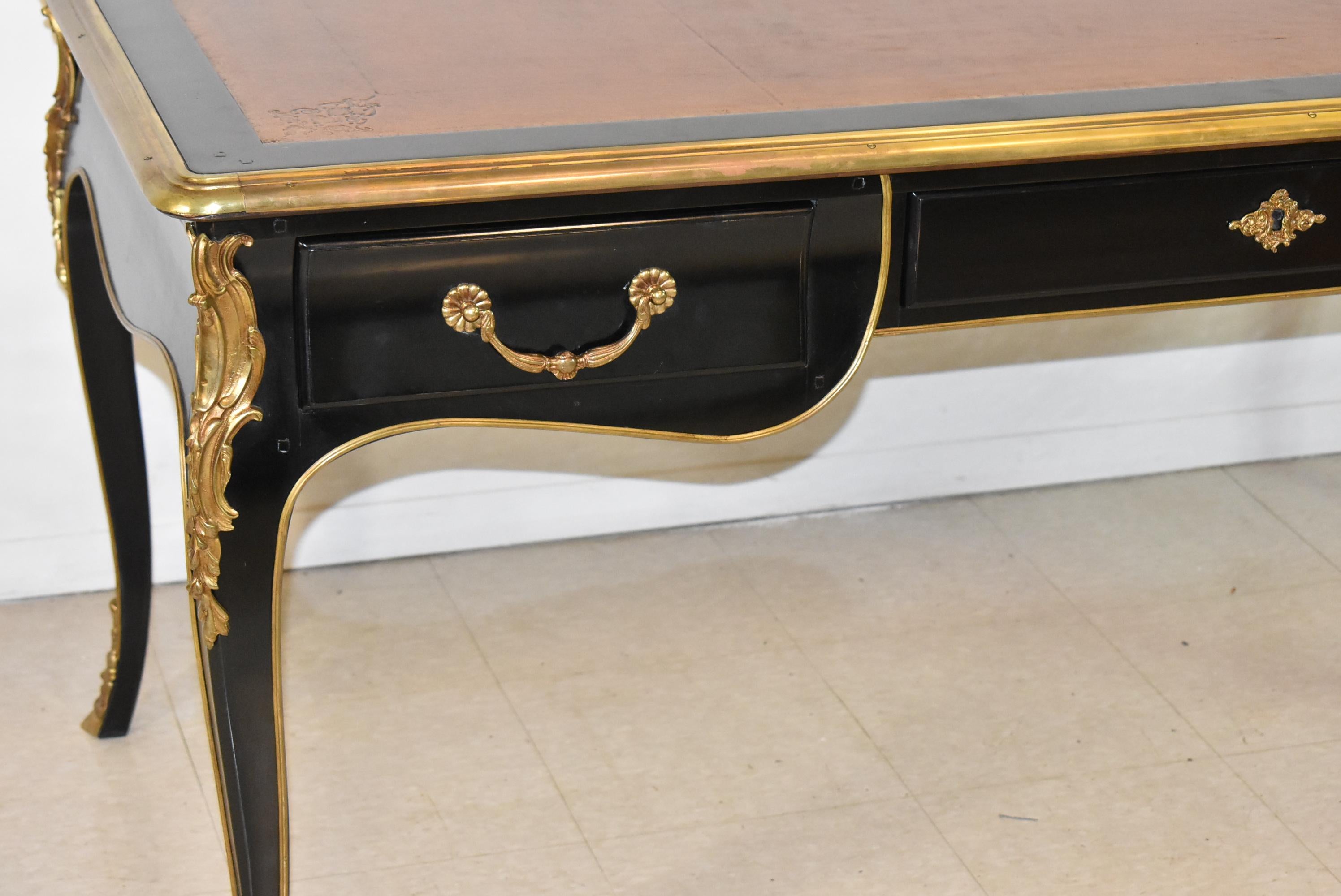 Scrivania in stile Luigi XV laccata di nero con gambe cabriole, montature in ottone e piedi a zoccolo. I 3 cassetti anteriori presentano una struttura a coda di rondine e maniglie in ottone pesante. La parte superiore in pelle marrone presenta am