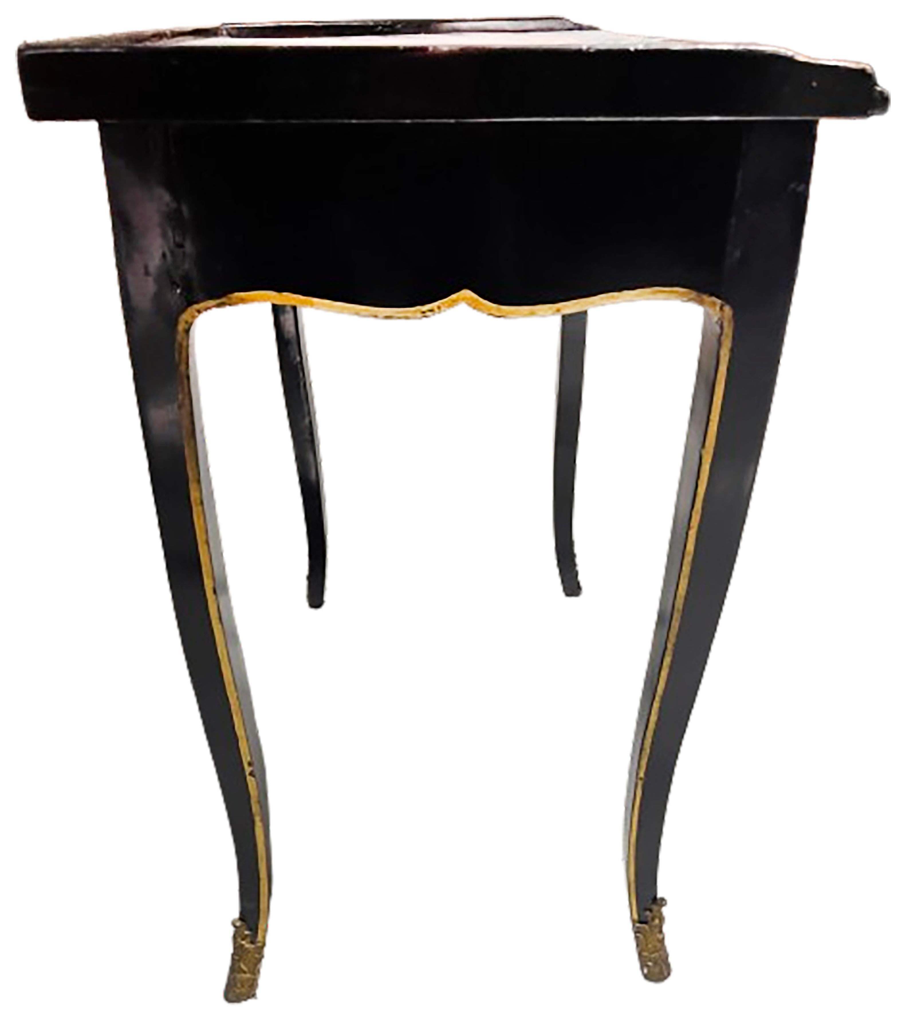 A handsome Louis XV style black lacquer painted wood table. Tooled crimson patinated leather top with gilt ormolu trim. Small gilt ornamentation pattern in the center as well as the corners of the leather. Graceful legs with gilt trim & bronze