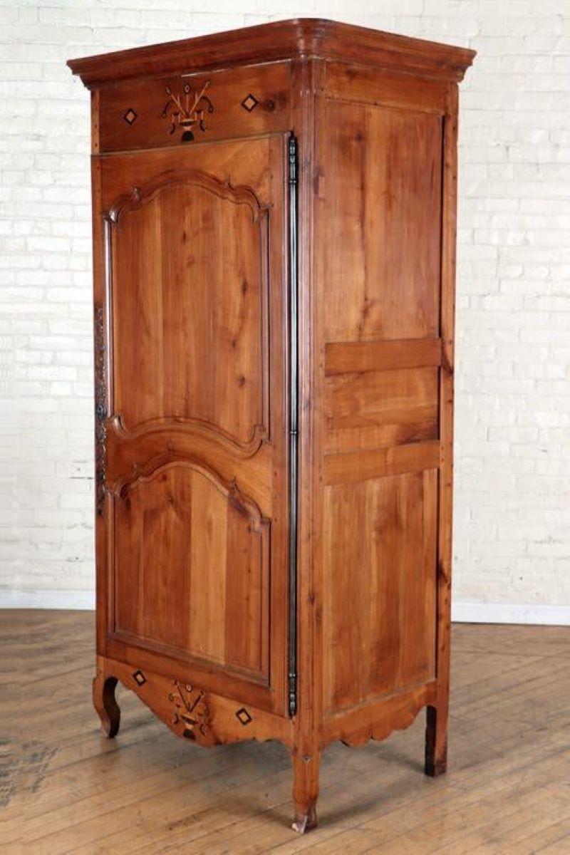 A charming Louis XV period bonnetiere armoire (designed to store wide-brimmed hats) in cherrywood, circa 1790, with inlaid ebony and other woods above and below the single paneled door. A simple crown and short cabriloe feet. The interior has been