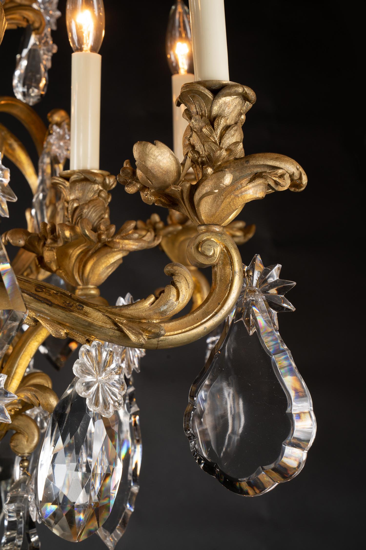 Questo magnifico lampadario rococò Luigi XV, con fusioni finemente cesellate, presenta coppe per candele e bobeches in bronzo d'ore con un centro in cristallo massiccio. Questo pezzo d'antiquariato francese risale al XIX secolo e possiede una