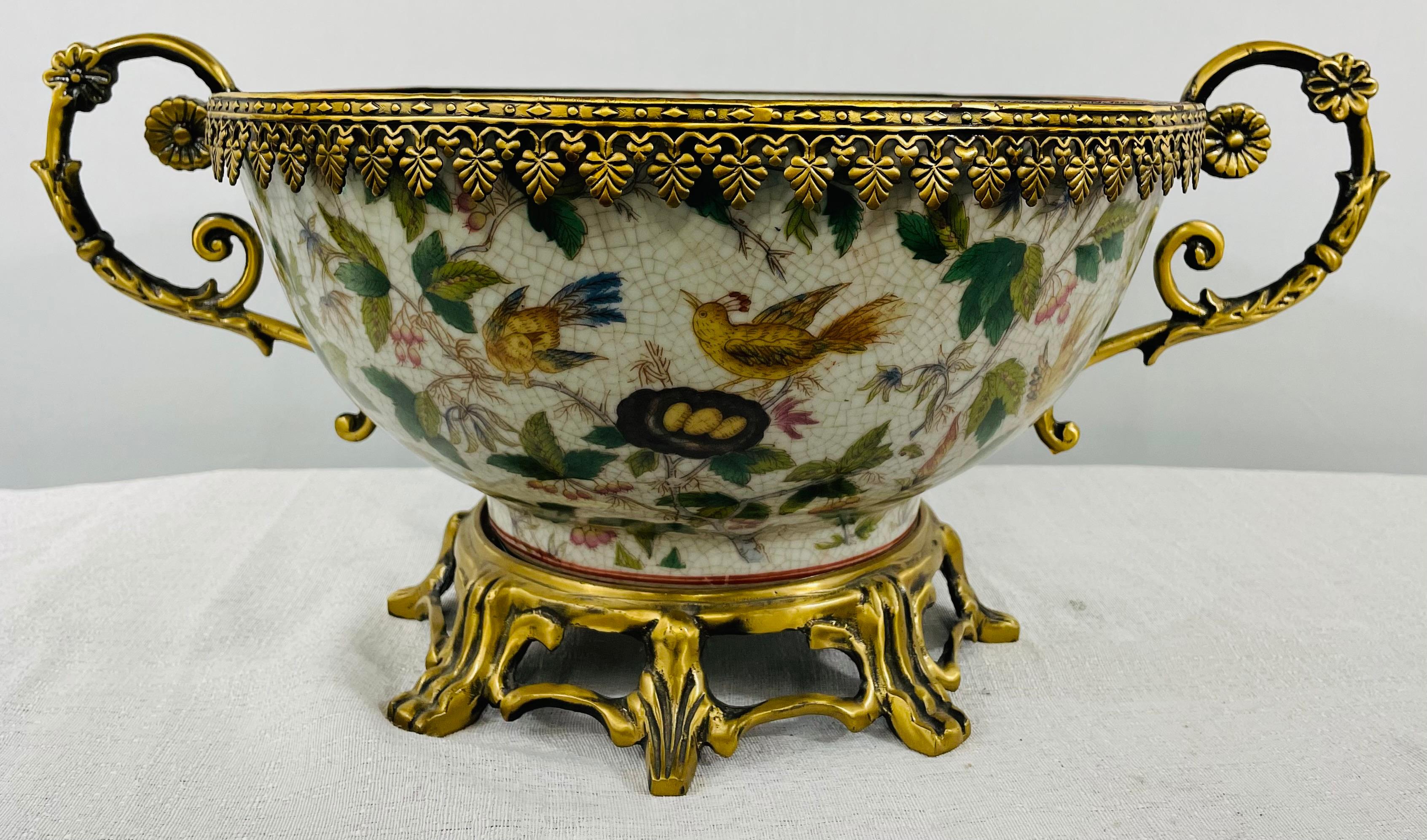 An exquisite Louis XV style bronze mounted Chinese Export centerpiece bowl. The porcelain bowl is finely hand painted with exotic birds, dragon fruits and plants. The bowl features two bronze handles with floral design, a rim in acanthus motifs and