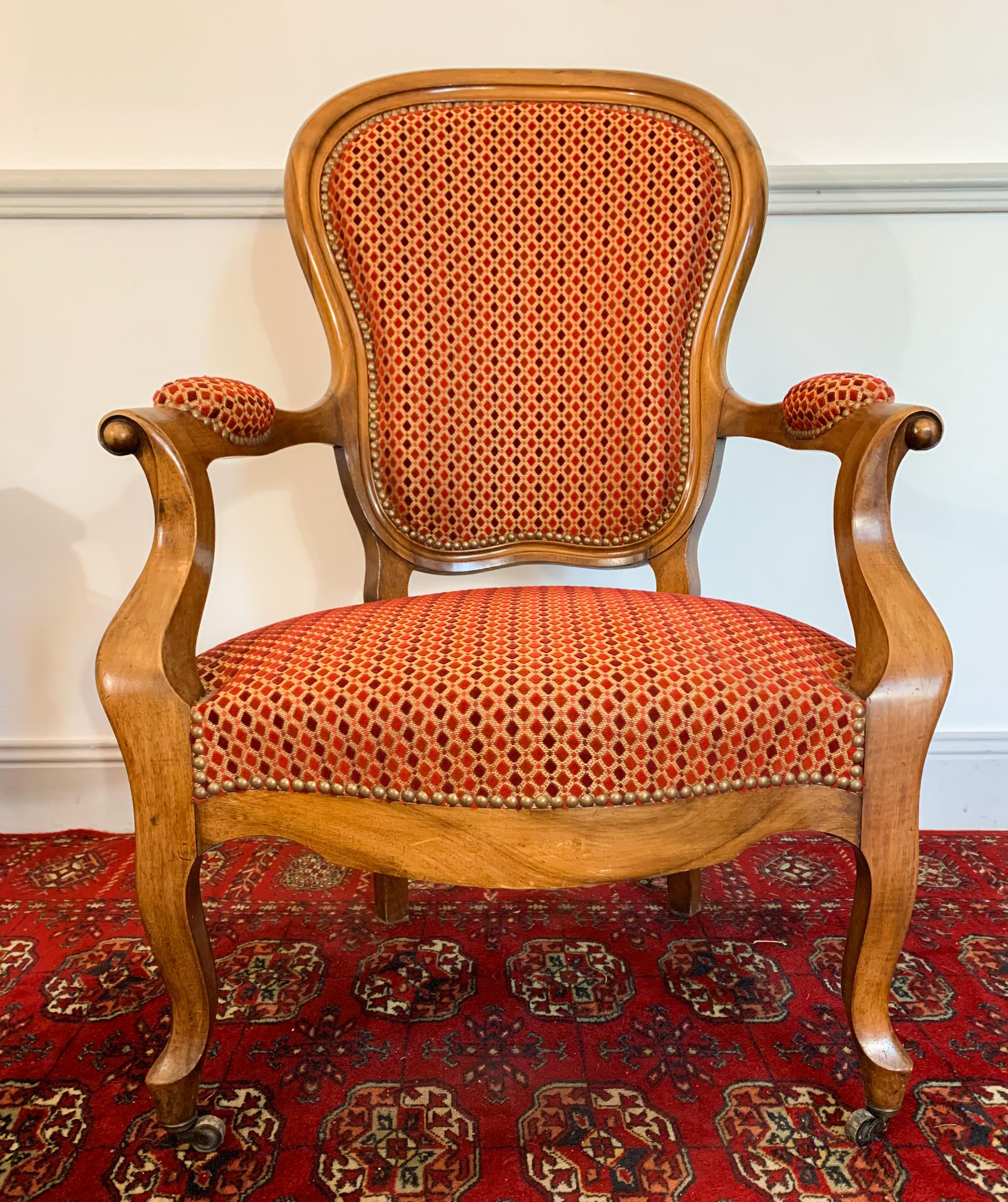 Beautifull Louis 15 style walnut cabriolet cabriolet from Louis-Philippe period. Its front legs are curved and end with casters. The armrests have volutes bringing a certain elegance. 
It has a beautiful red and orange embossed velvet tapestry.