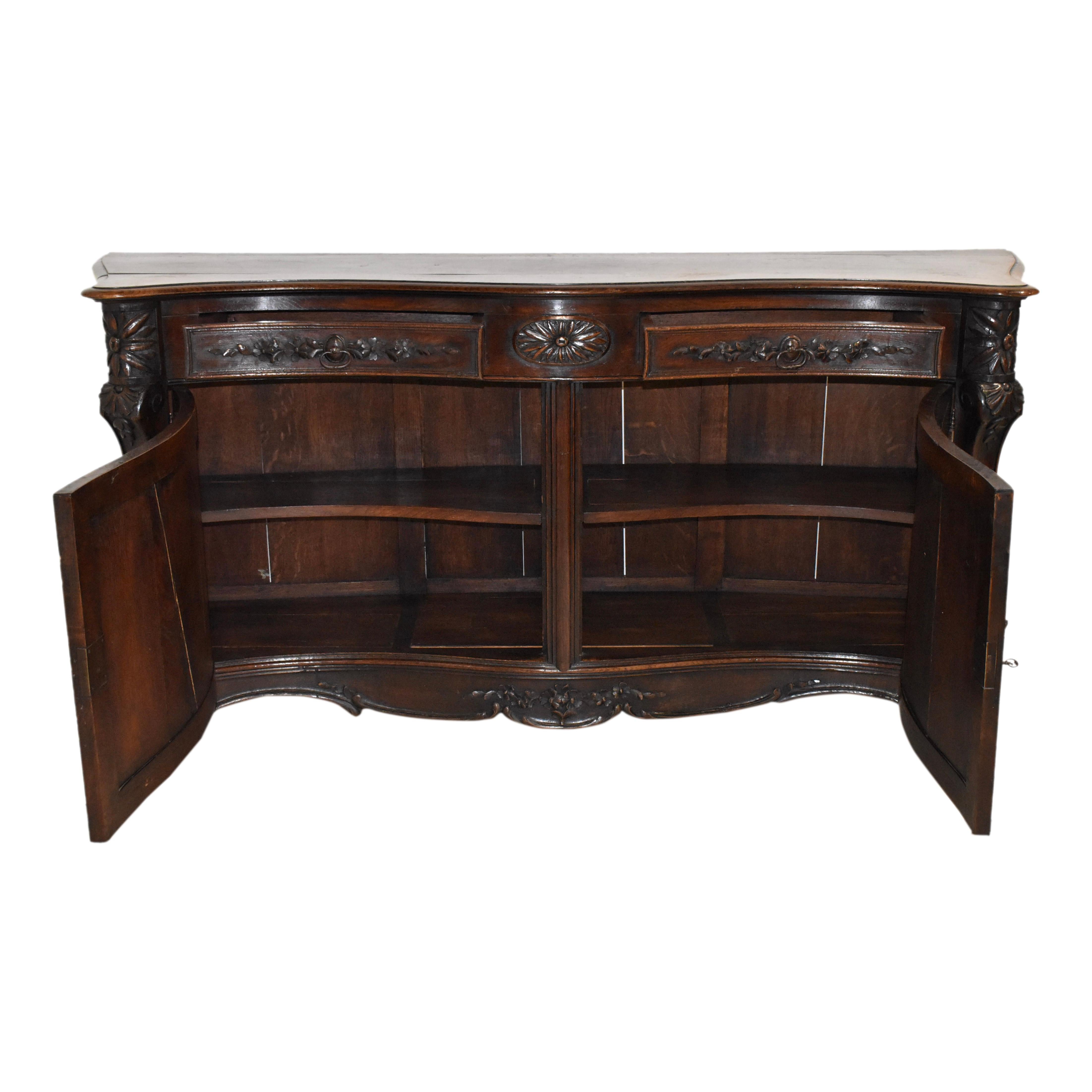 The graceful lines of a serpentine front, rounded corners, cabriole legs, and scrolled carvings are paired with solid oak construction finished in a dark stain with a lovely patina, creating this magnificent sideboard that is both elegant and bold.