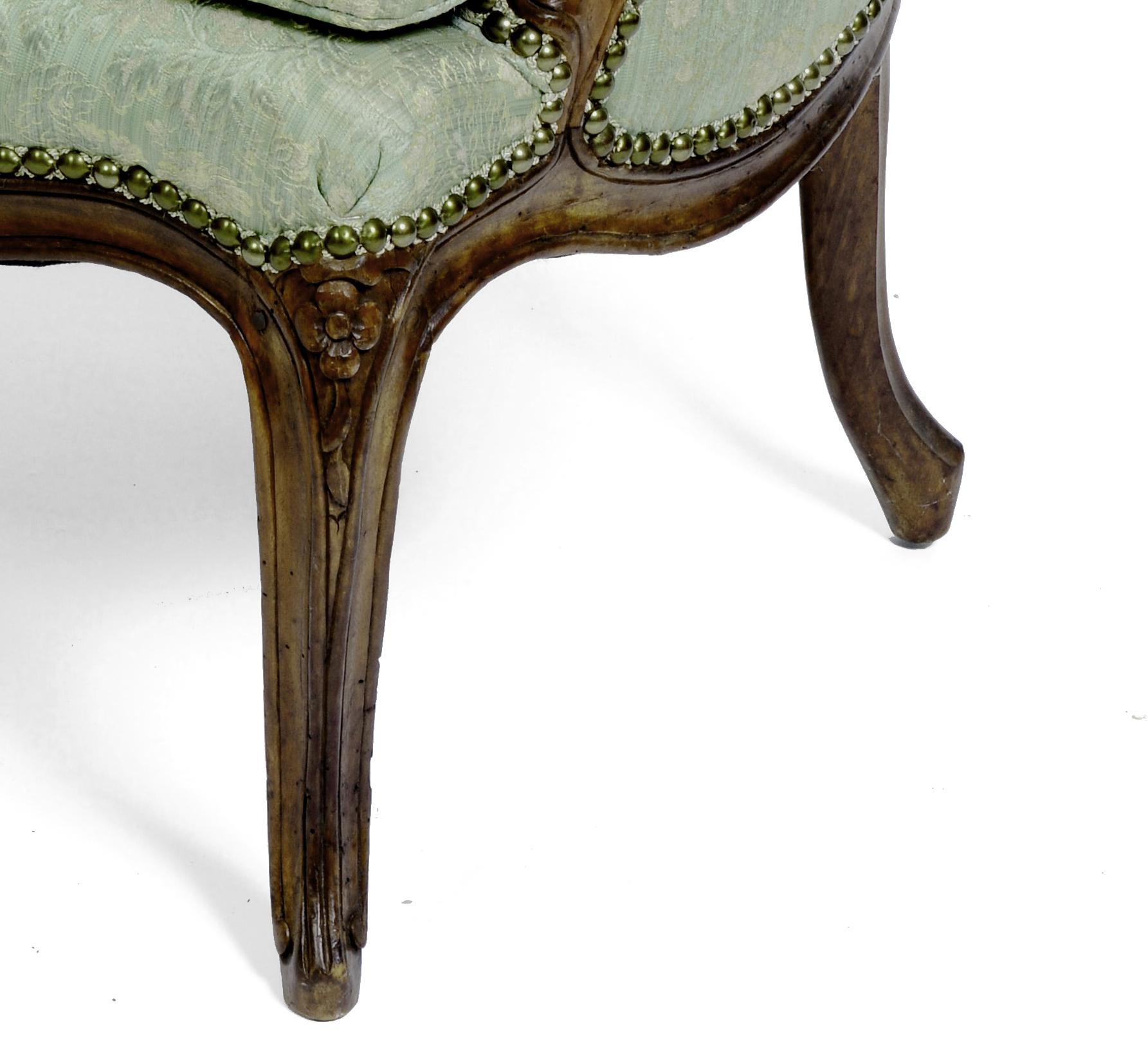 This graceful French bergère is made of floral carved walnut with a curved back and apron. The chair has a generously scaled seat with a tailored loose seat cushion and stands on carved cabriolet legs. A comfortable and stylish chair for any room