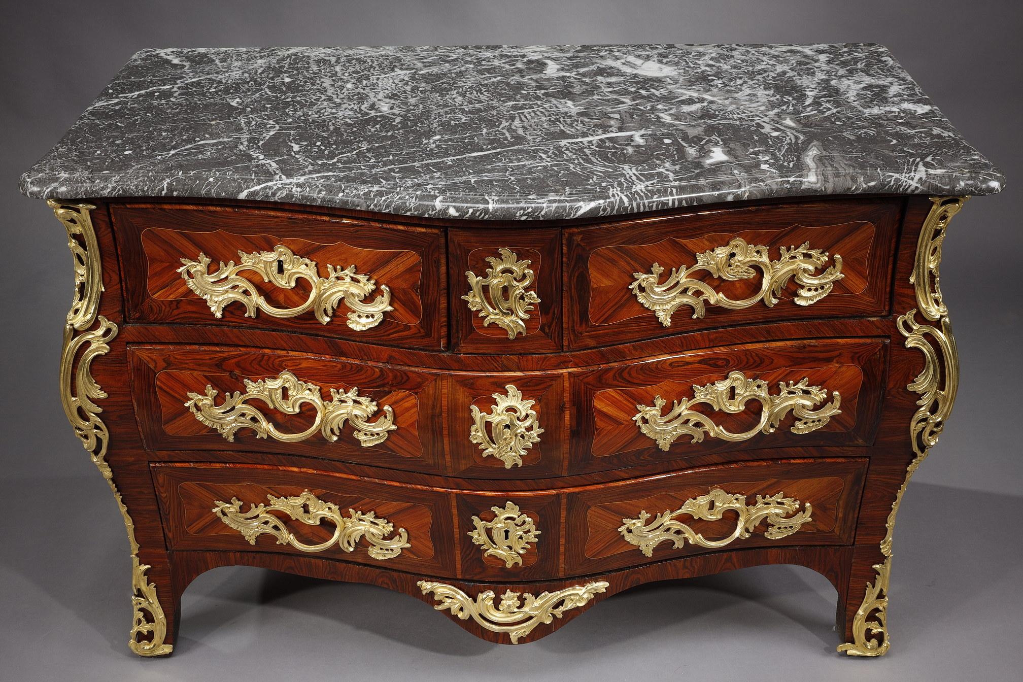 Louis XV period chest of drawers in wood veneer. The front
opens up to five drawers on three rows. It rests on straight legs. The piece is richly decorated with ormolu and chiseled rocaille on the entrances of the lock, the handles of the drawers