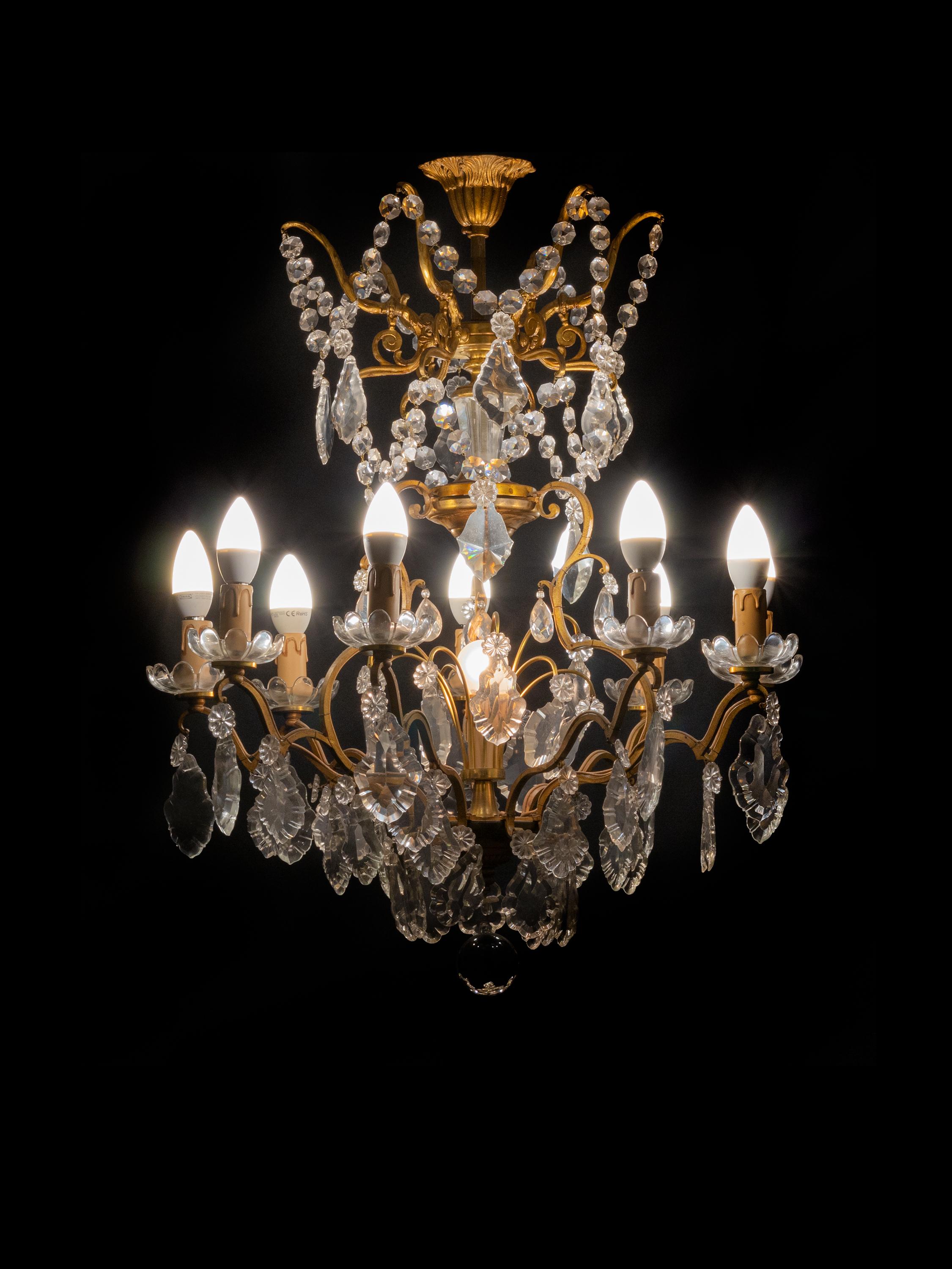A Classic Louis XV style chandelier having 9 arms and 10 lamps (9 lamps and 1 central lamp).
The gilt metal frame heavily laden with various sized crystal plaquettes.
Originally candle lit but now completely electrified. 
Electric Installation