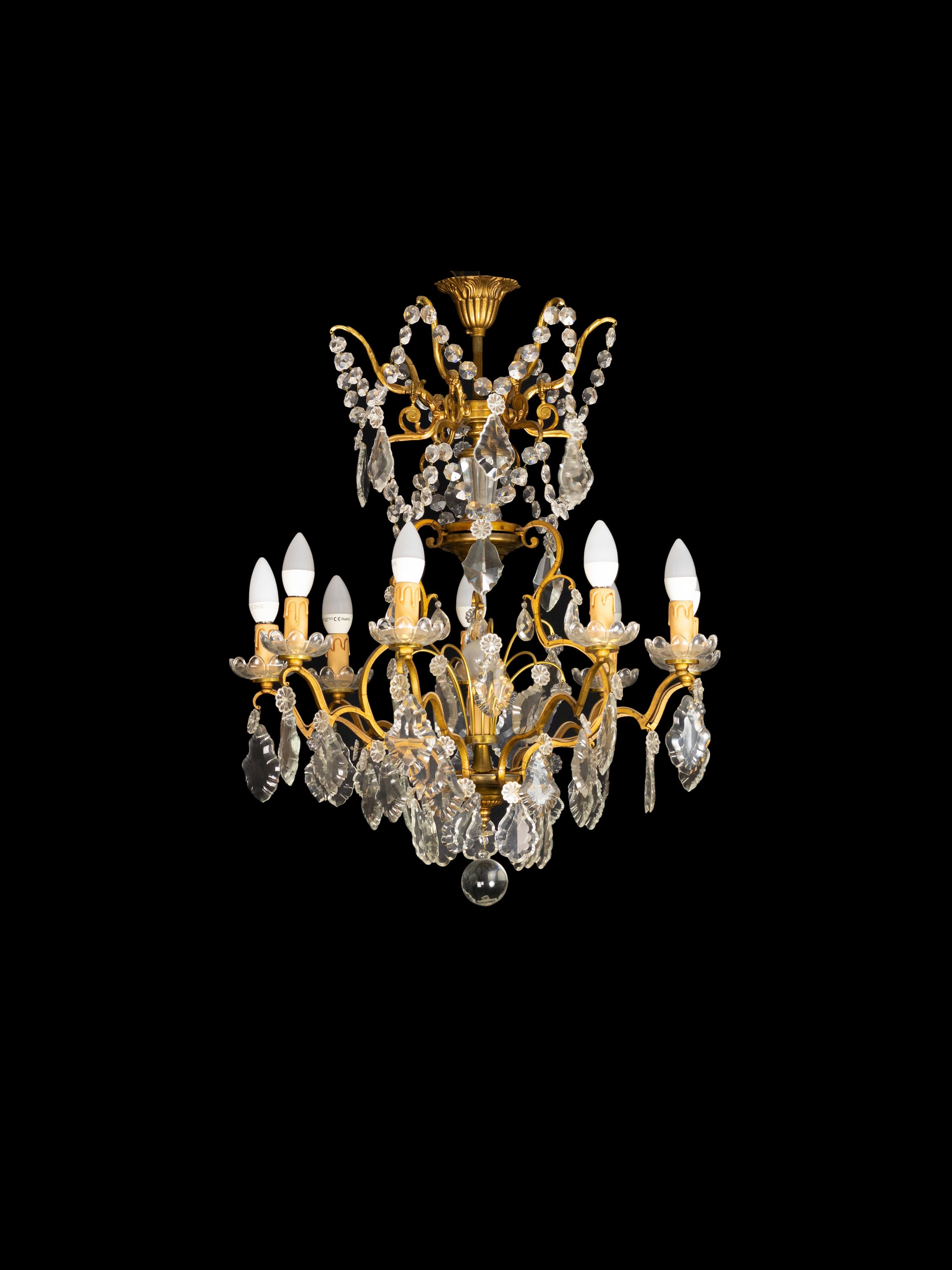 A Classic Louis XV style chandelier having 9 arms and 10 lamps (9 lamps and 1 central lamp).
The gilt metal frame heavily laden with various sized crystal plaquettes.
Originally candle lit but now completely electrified. 
Electric Installation